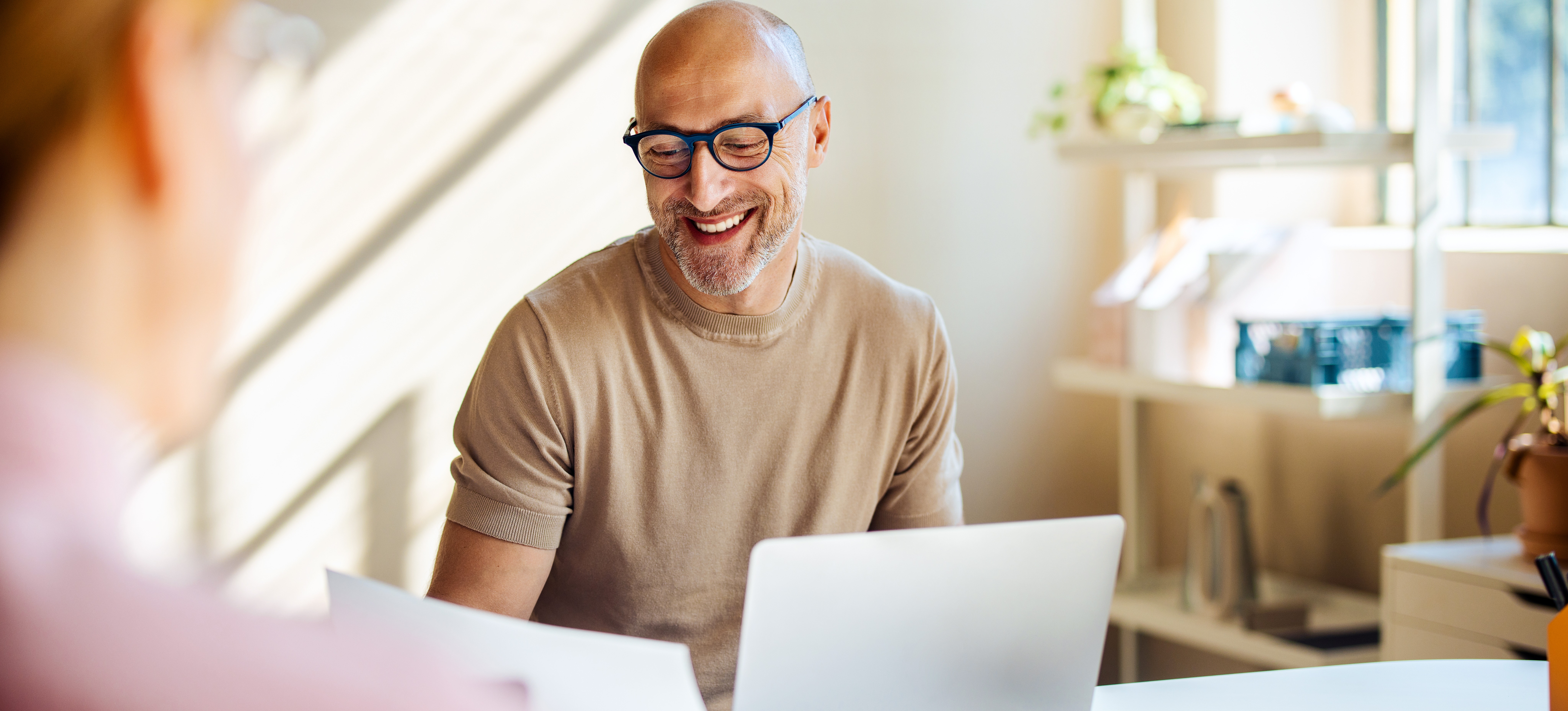 [Feature Image] A professional in dark-rimmed glasses smiles while looking at a paper instructing them how to sync Google Sheets with Google Calendar.