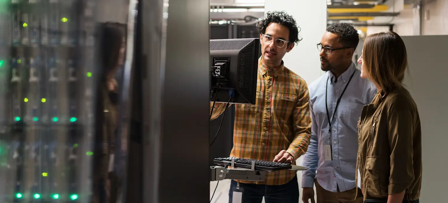 [Featured image] Three security engineers examining data security protocols on a computer monitor inside a server room.
