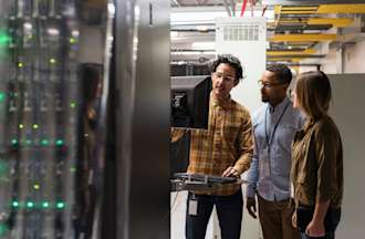 [Featured image] Three security engineers examining data security protocols on a computer monitor inside a server room.