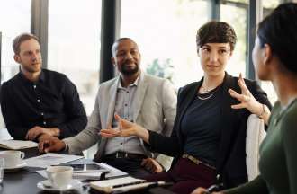 [Featured image] Two women and two men sit at a conference table discussing business marketing.