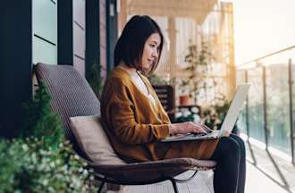 [Featured image] A woman sits on an outdoor patio with her laptop in her lap working on her portfolio