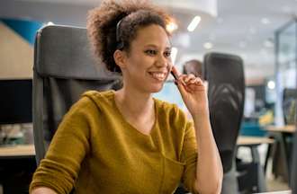 [Featured Image] An office worker smiles while taking a call at their entry-level help desk job.