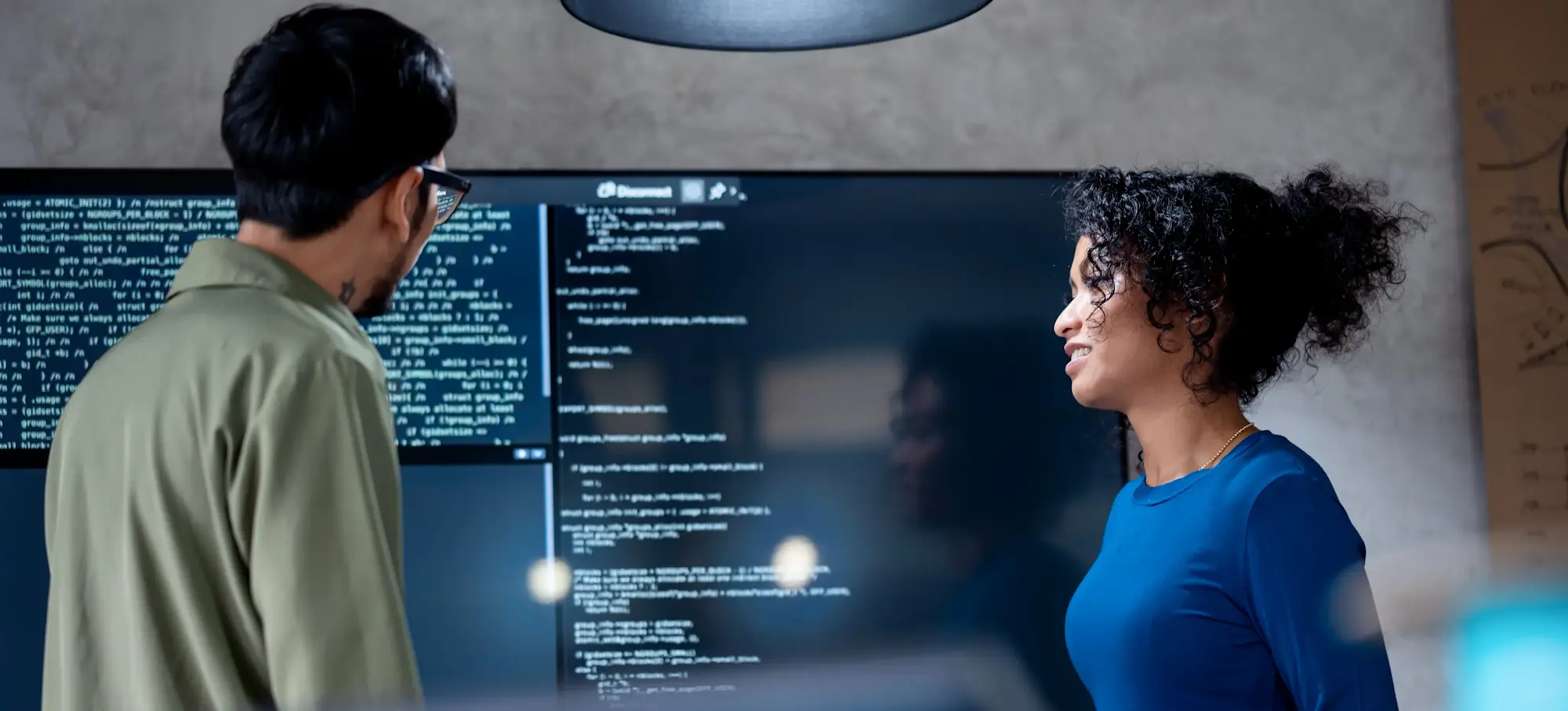 [Featured Image: Two programmers in front of a large screen discuss the top languages for machine learning.]
