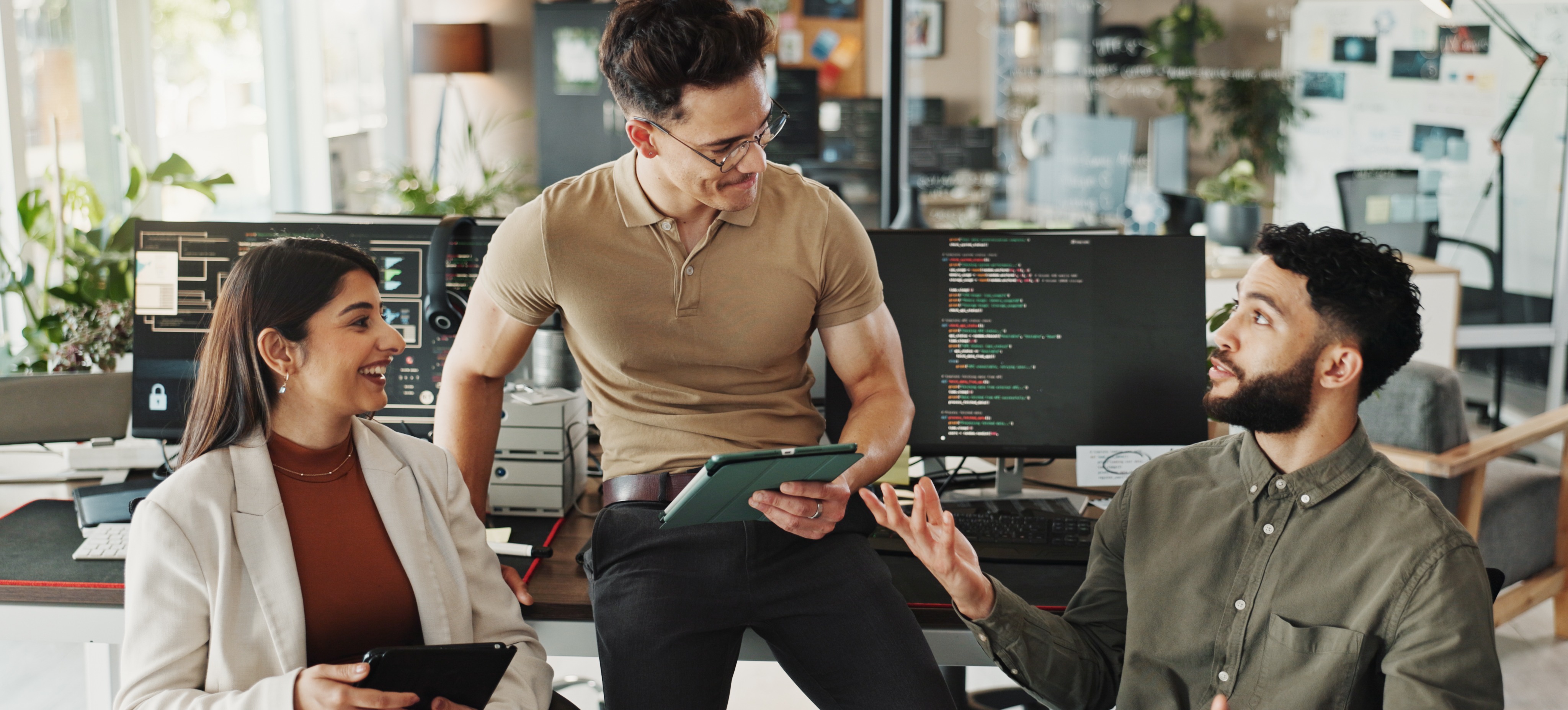 [Feature Image] A cybersecurity manager meets with two team members to discuss strategies in front of their workspaces.
