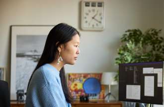 [Featured Image]: A woman with long dark hair, wearing a blue sweater. She is sitting in front of her computer,  analyzing data for the health care organization she works for. 