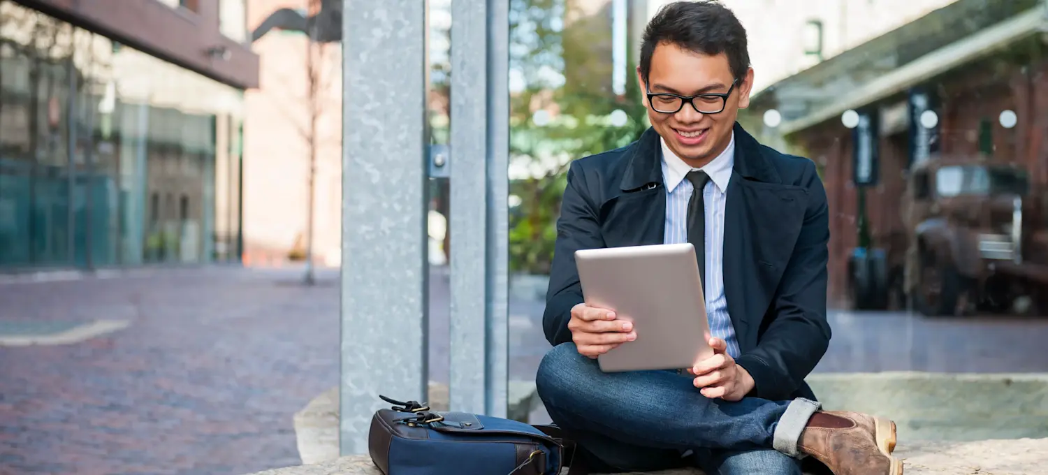 [Featured Image] A person is sitting outside using their tablet. 