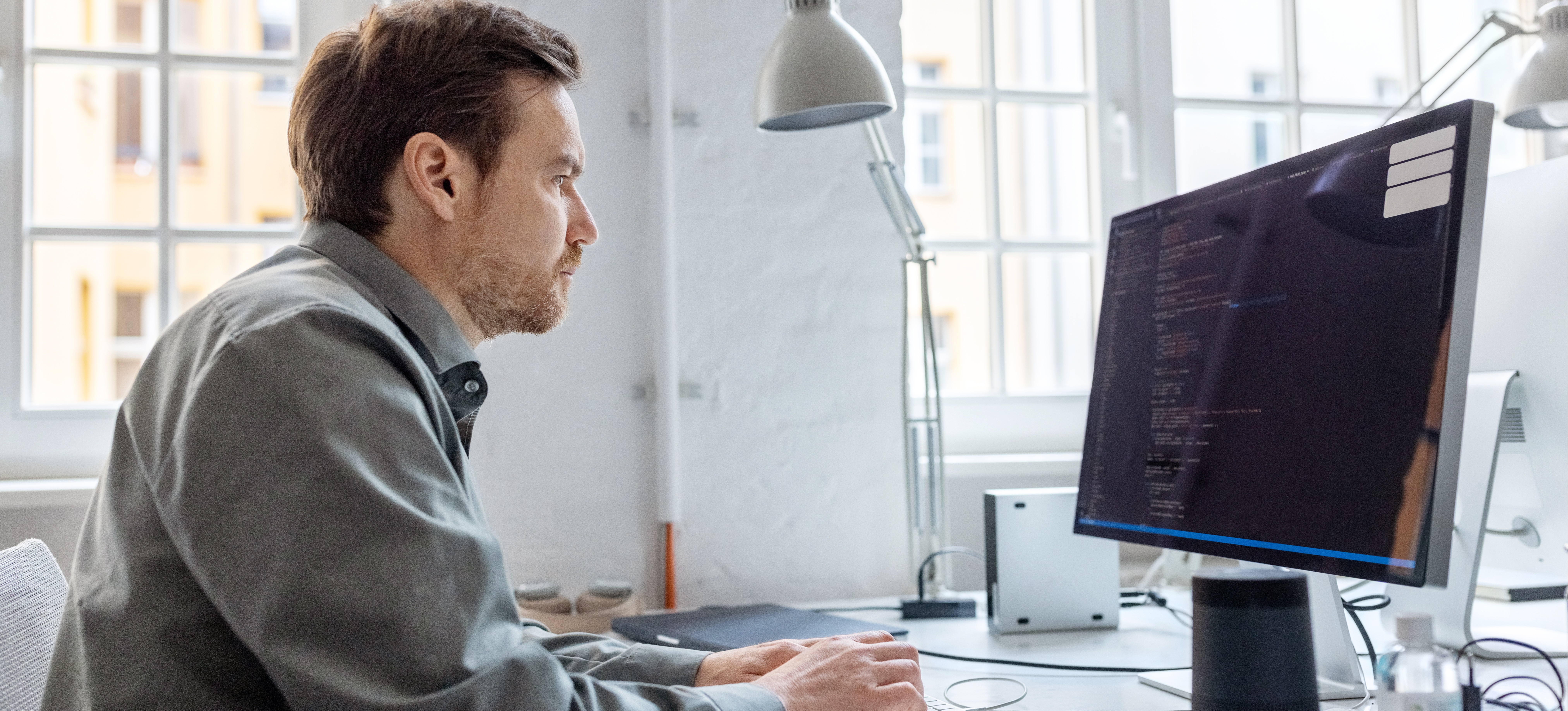 [Featured Image] A male Python developer sits at his desktop computer and helps with an organization's technological framework.