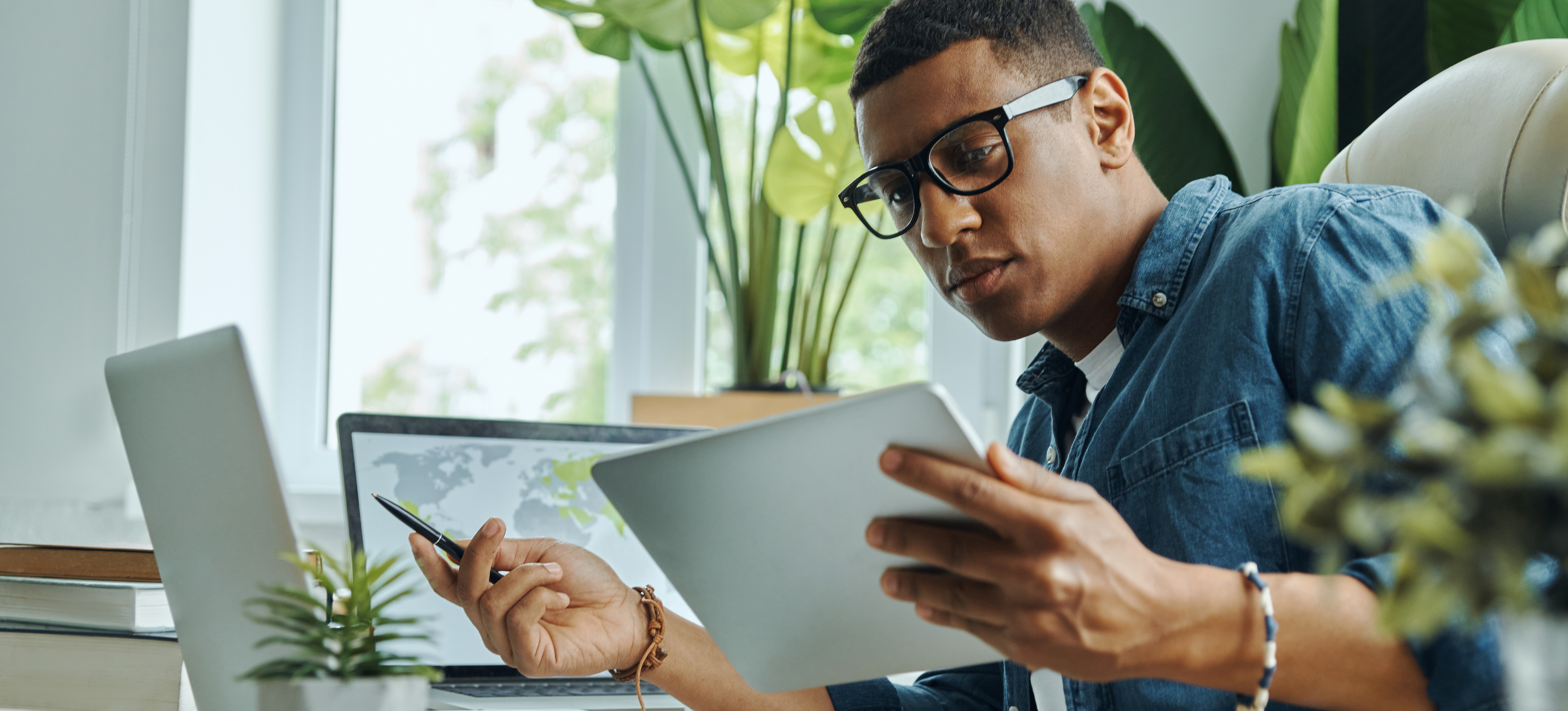 [Featured Image] A machine learning engineer analyzes data using VAEs while looking at a handheld device and two laptops in a sunny office.