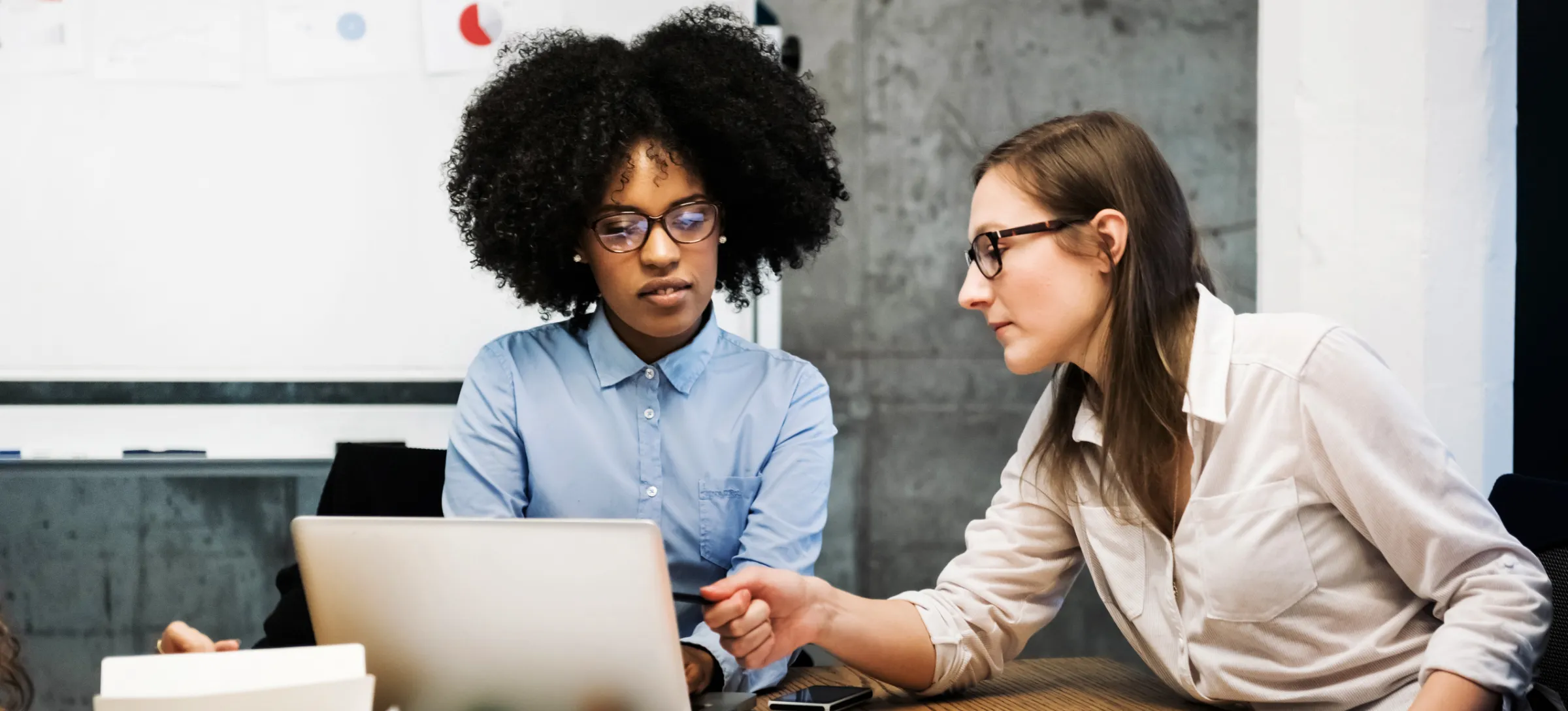 [Featured Image] An enterprise architect walks a new employee through some of the tasks they will handle as part of the team as they review content on a laptop with a whiteboard in the background. 
