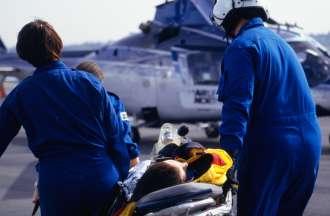[Featured image] A flight nurse and crew carry a patient on a stretcher toward a helicopter for transport to a hospital.