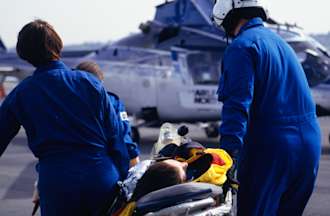 [Featured image] A flight nurse and crew carry a patient on a stretcher toward a helicopter for transport to a hospital.