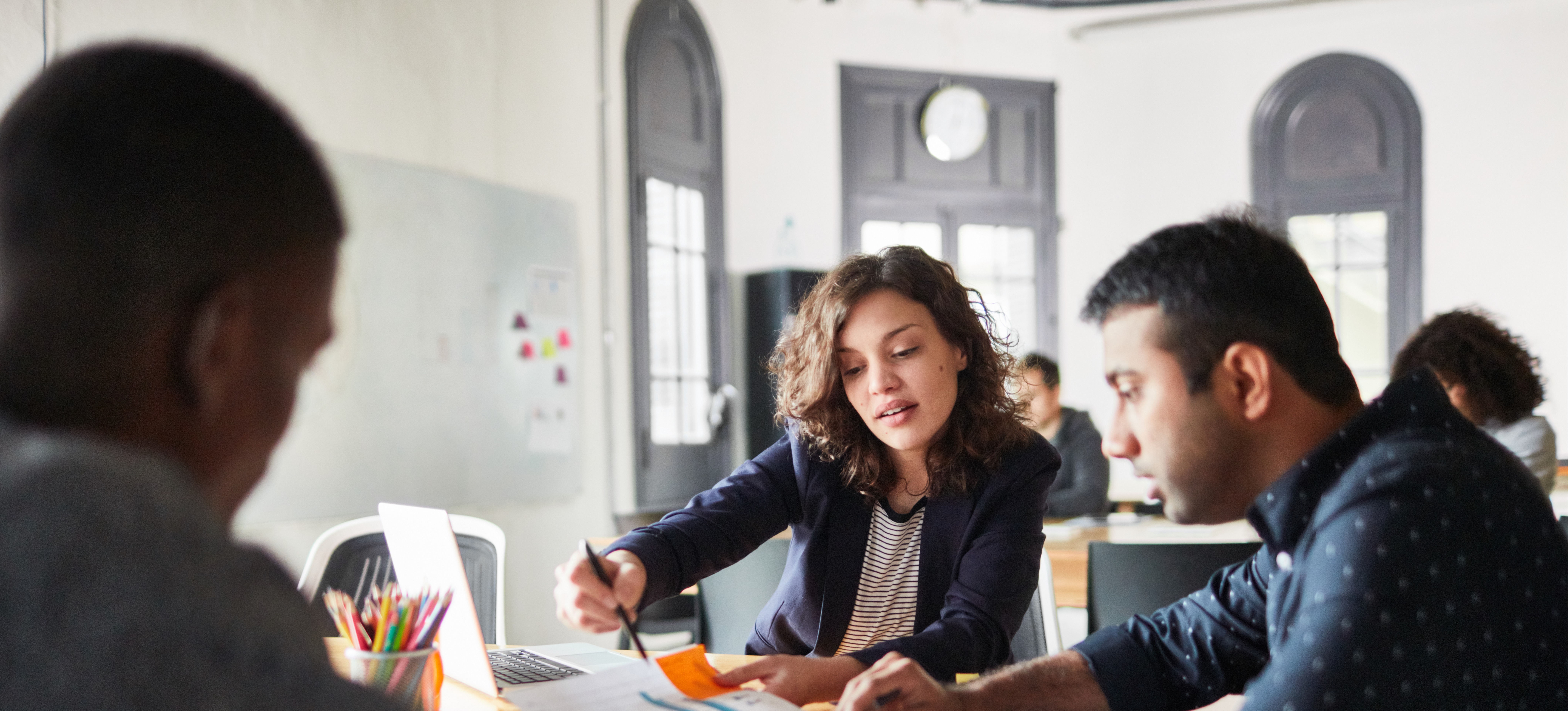 [Featured image] Two colleagues are working in front of a desktop as they discuss the change management process. 