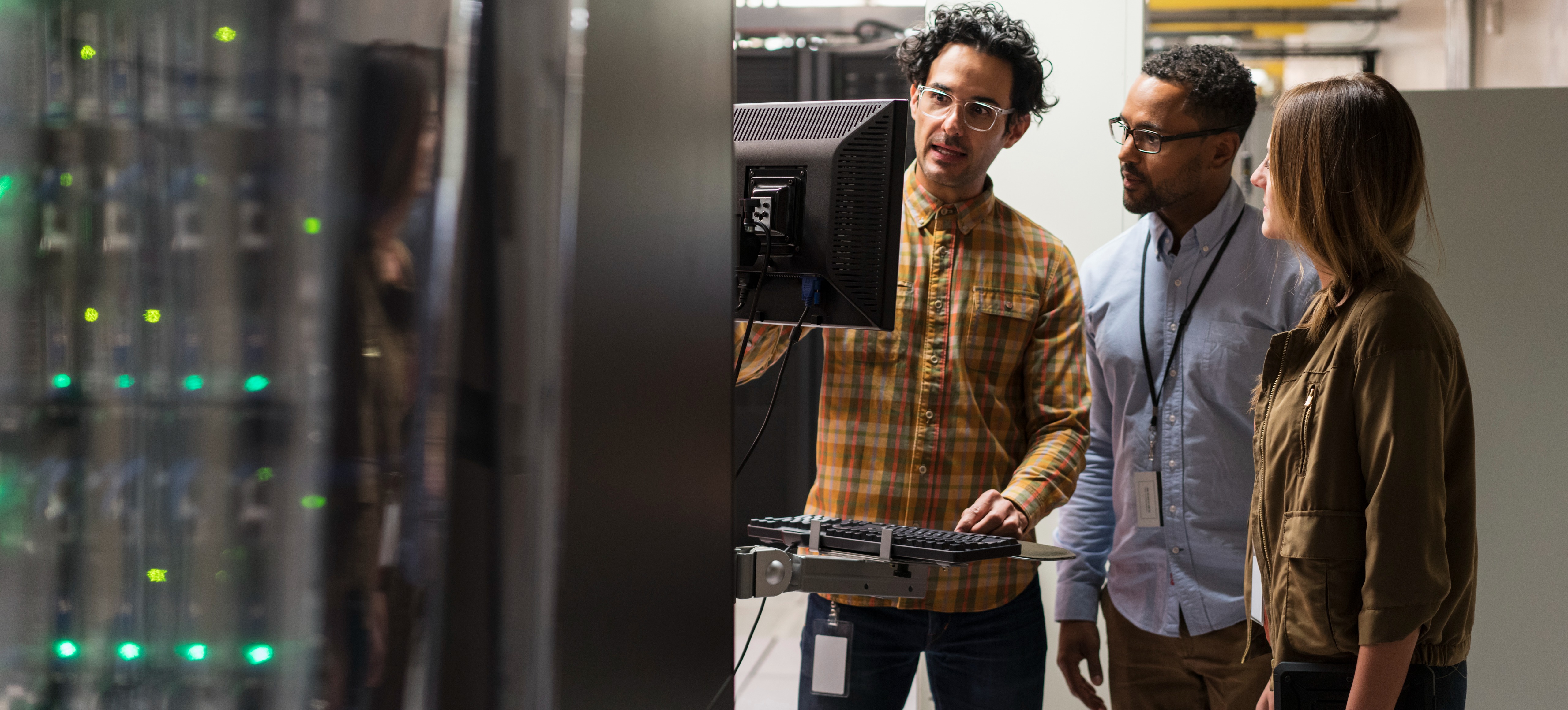 [Featured image] Three security engineers examining data security protocols on a computer monitor inside a server room.