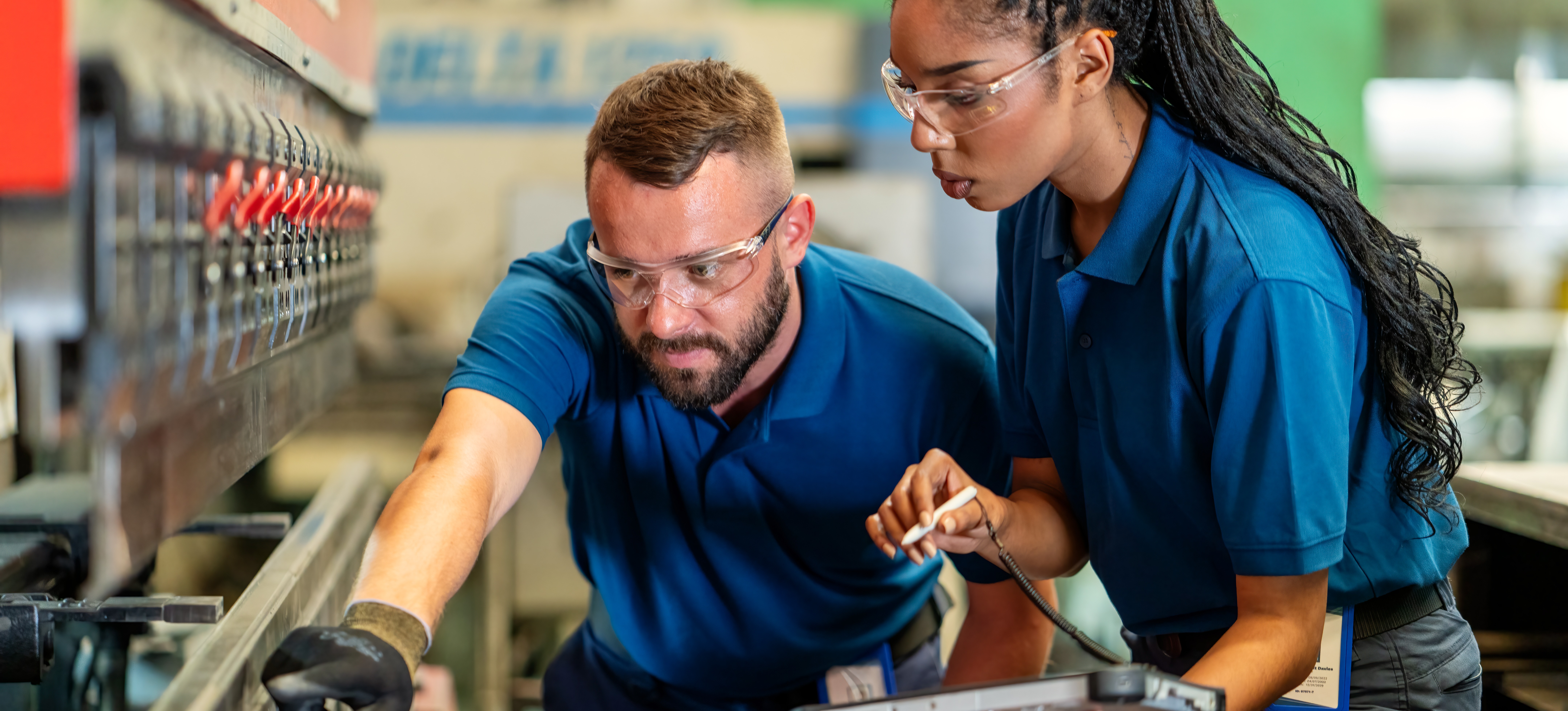 [Featured Image] An apprentice who has sought alternatives to college is holding a tablet while inspecting factory machinery with their trainer.
