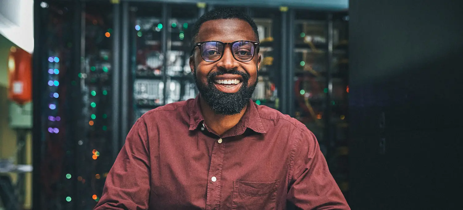 [Featured Image]:  A person, wearing a reddish shirt, glasses.  They are working in front of their computer in their office.  