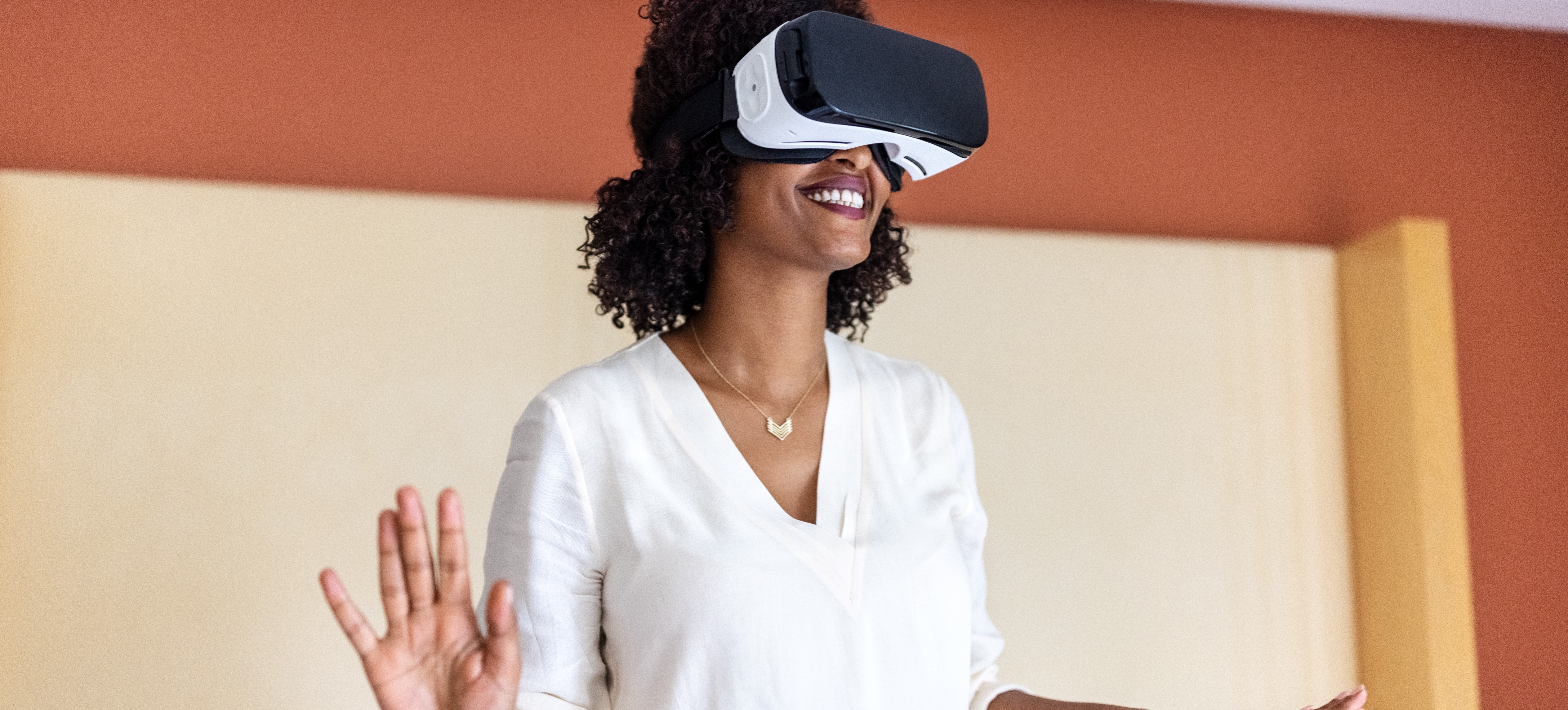 [Hauptbild] Eine lächelnde Frau verwendet ein VR-Headset in einem farbenfrohen Raum.
