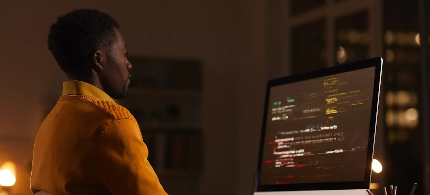 [Featured image] A quality assurance tester reviews units of code on a computer screen in a darkened room.
