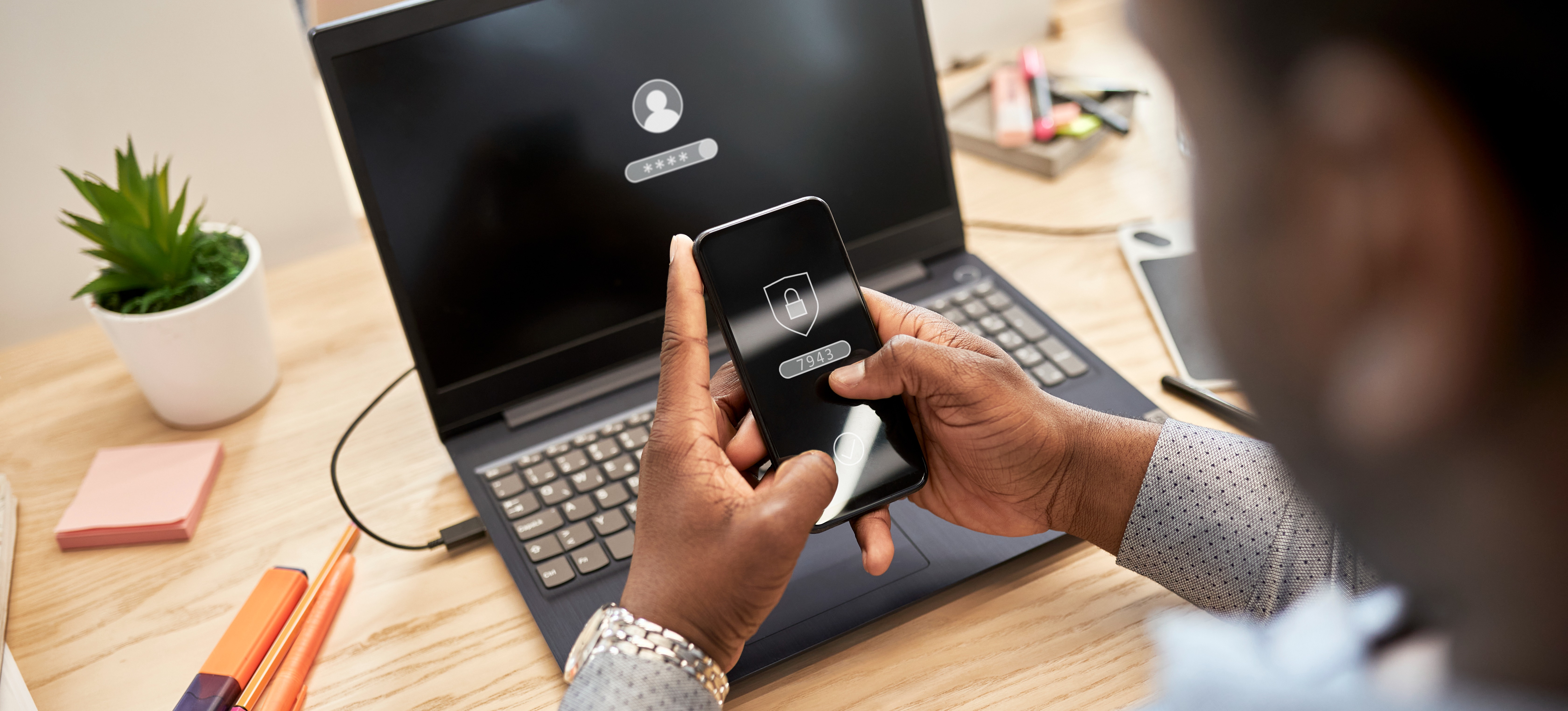 [Featured Image] A business person is using their smartphone to gain access to a password-protected website on their laptop that is instituting zero trust security measures.
