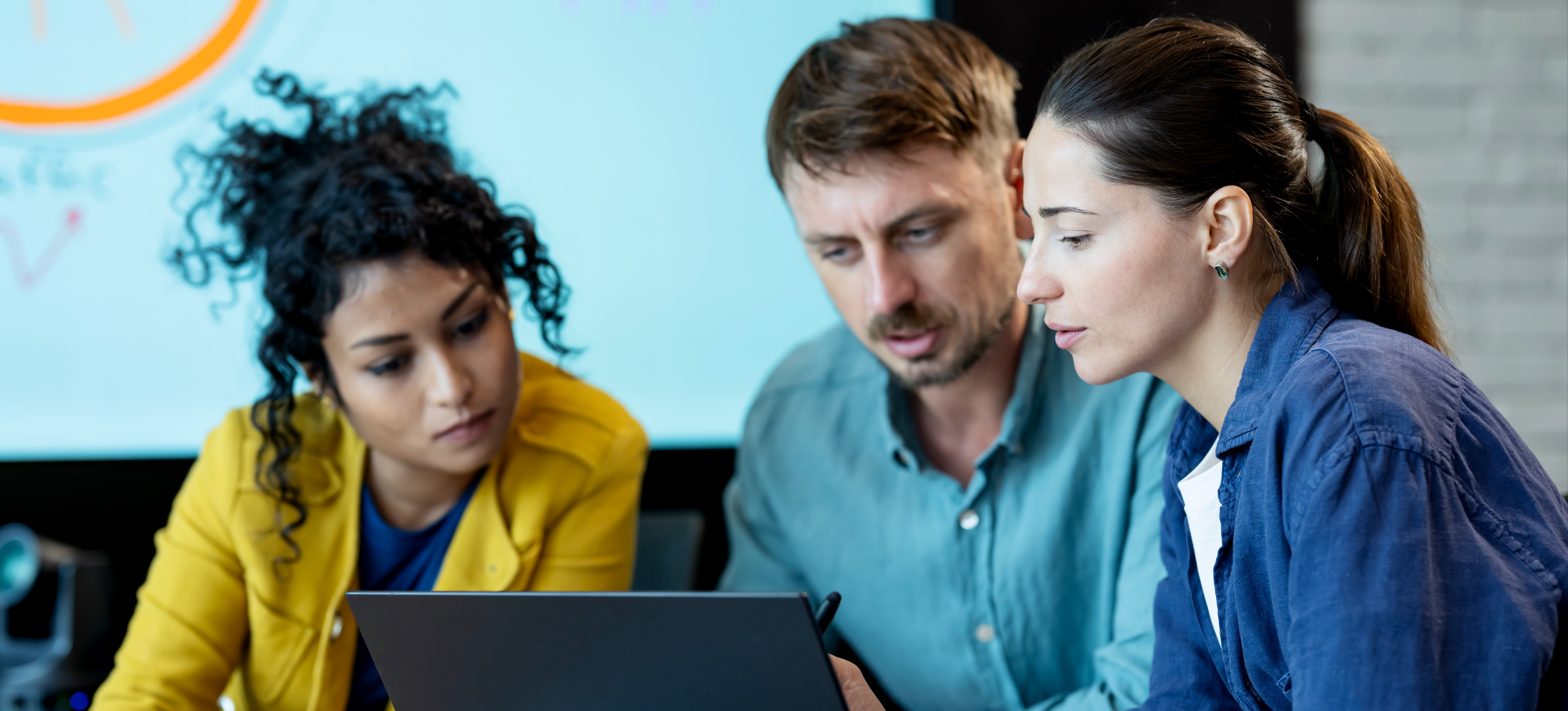 [Featured Image]: Three coworkers look at a laptop as they create a market penetration strategy.

