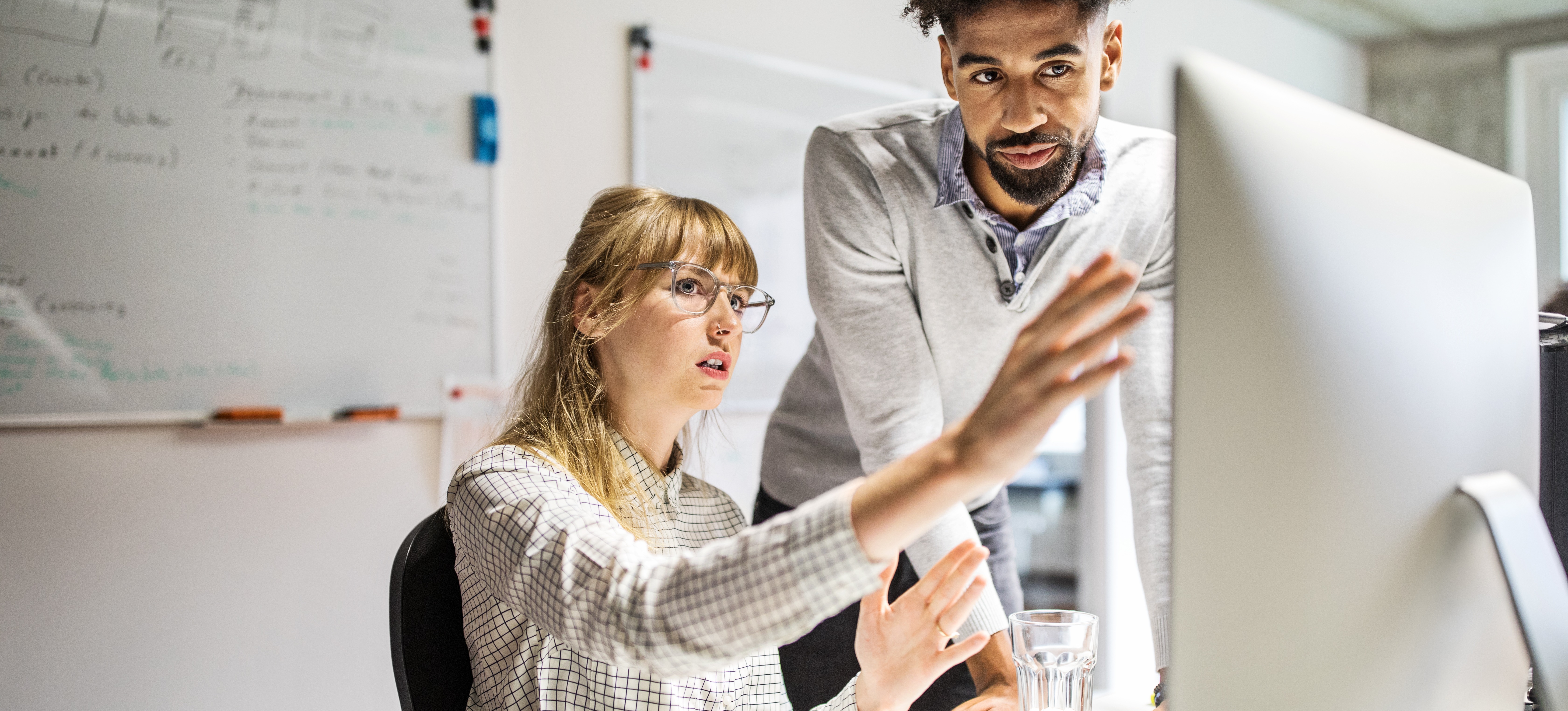 [Featured Image] Two machine learning engineers discuss pattern recognition while looking at a computer monitor. 
