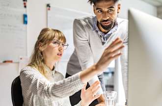 [Featured Image] Two machine learning engineers discuss pattern recognition while looking at a computer monitor. 
