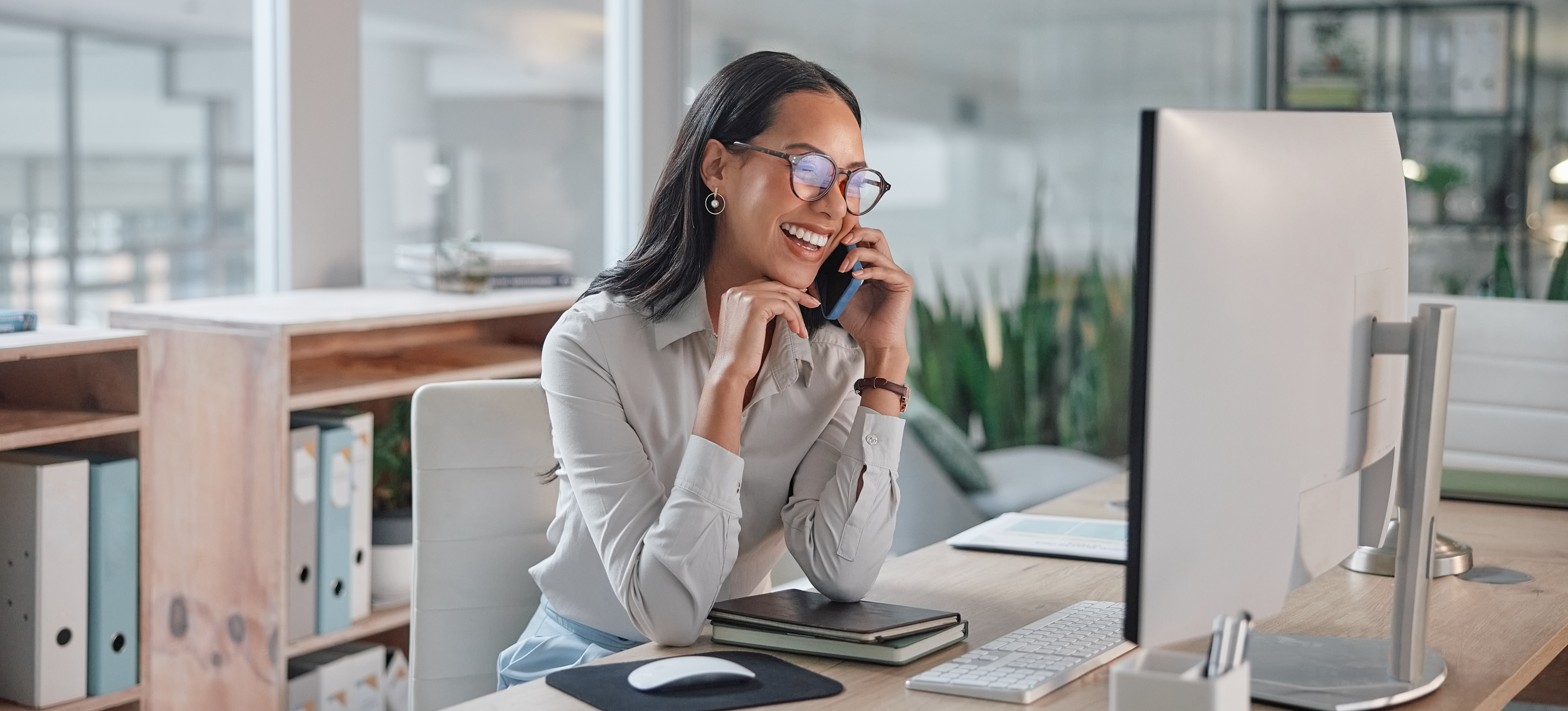 [Featured Image] A marketing professional sits at a computer and talks on the phone about the Google Ads remarketing program she implemented.   