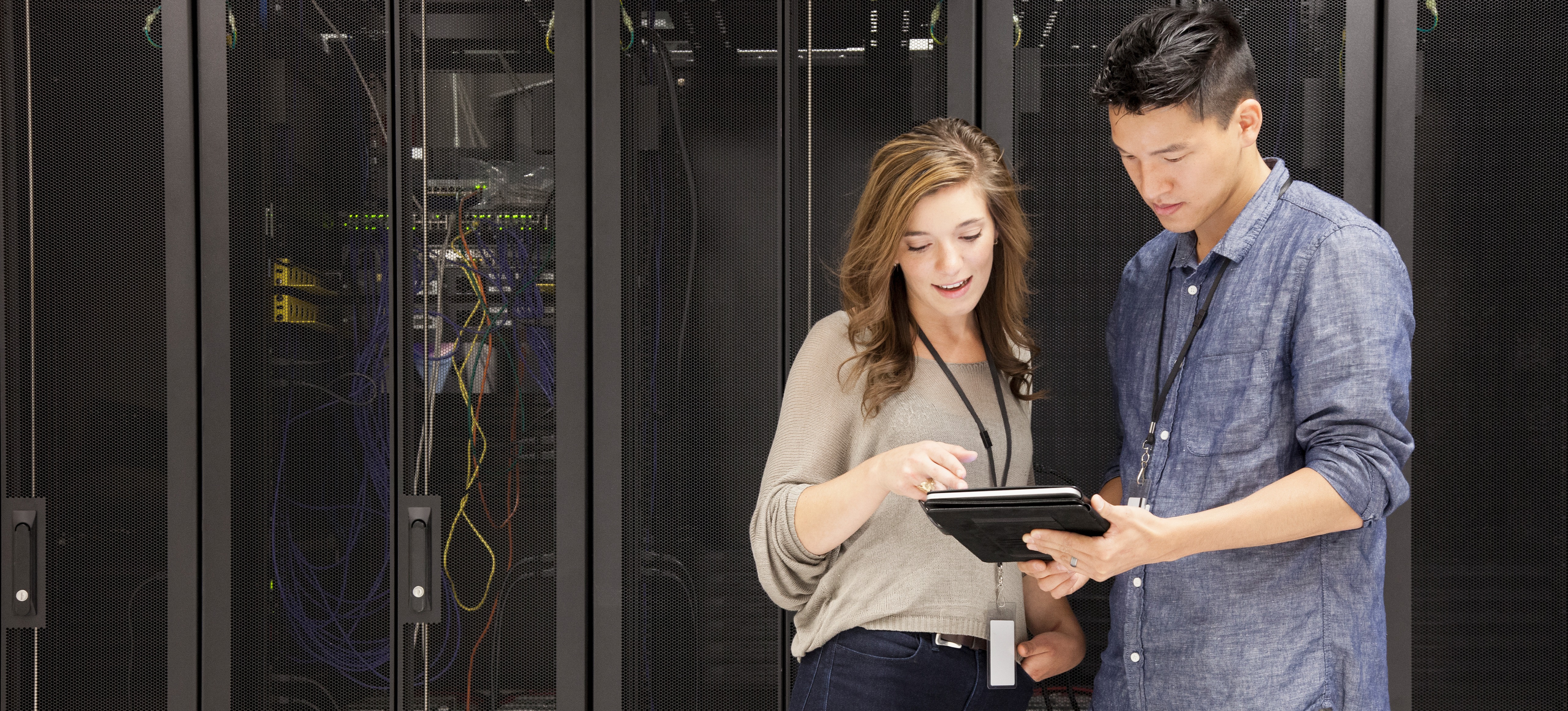 [Featured Image] Two penetration testers stand in a server room and discuss white hat testing as they look at a tablet.
