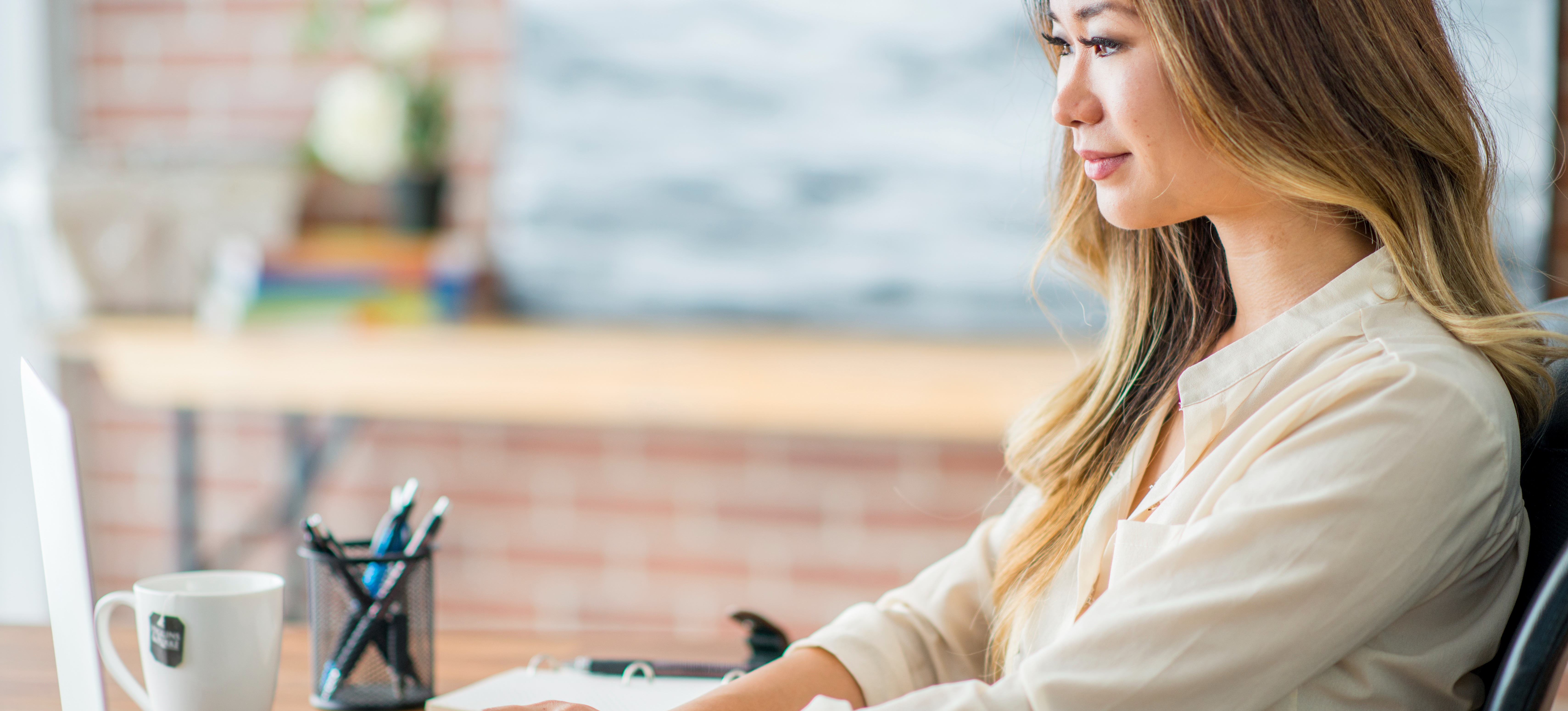 [Featured Image] A digital marketing specialist wearing a white blouse sits at her laptop in a modern office setting.
