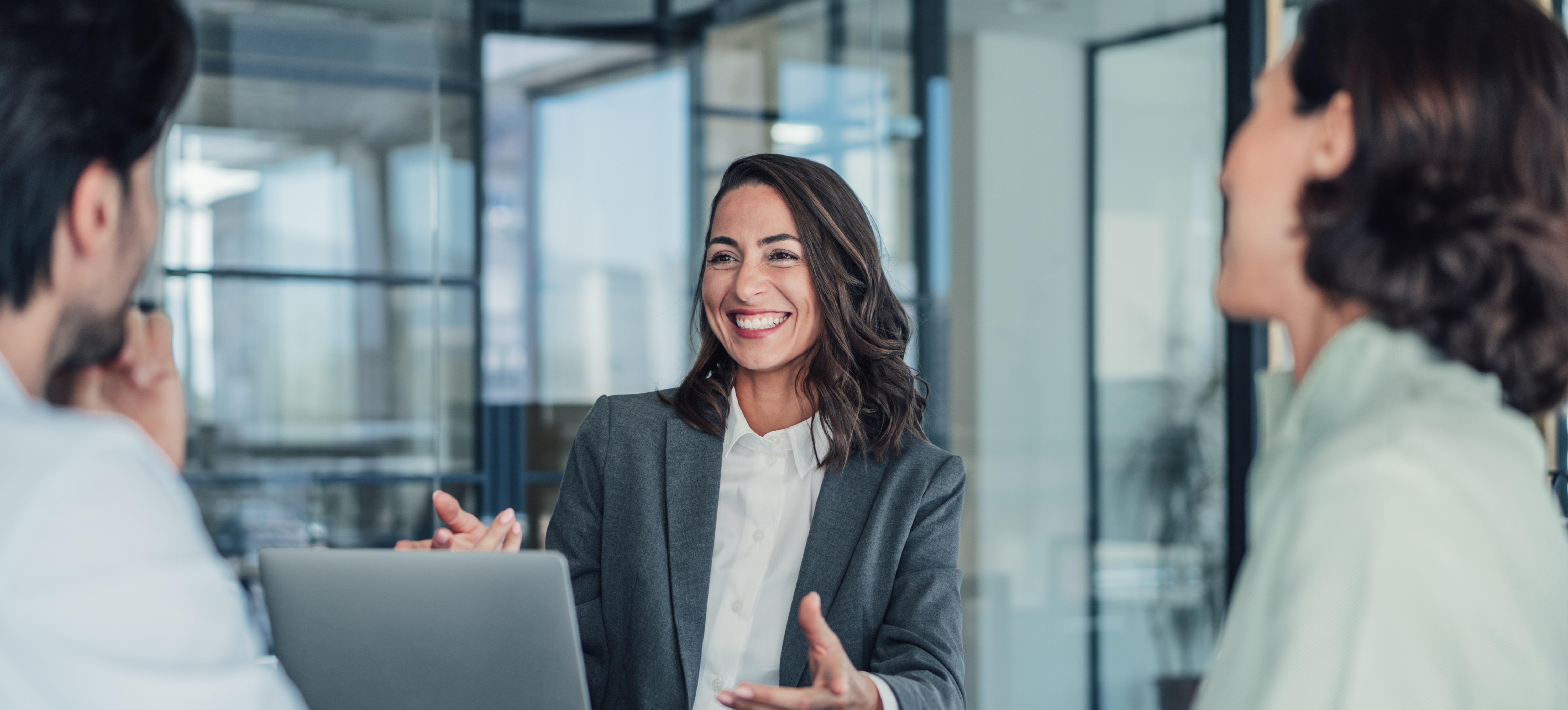 [Featured Image] An HR professional using online HR tools while discussing with colleagues in a professional environment.
