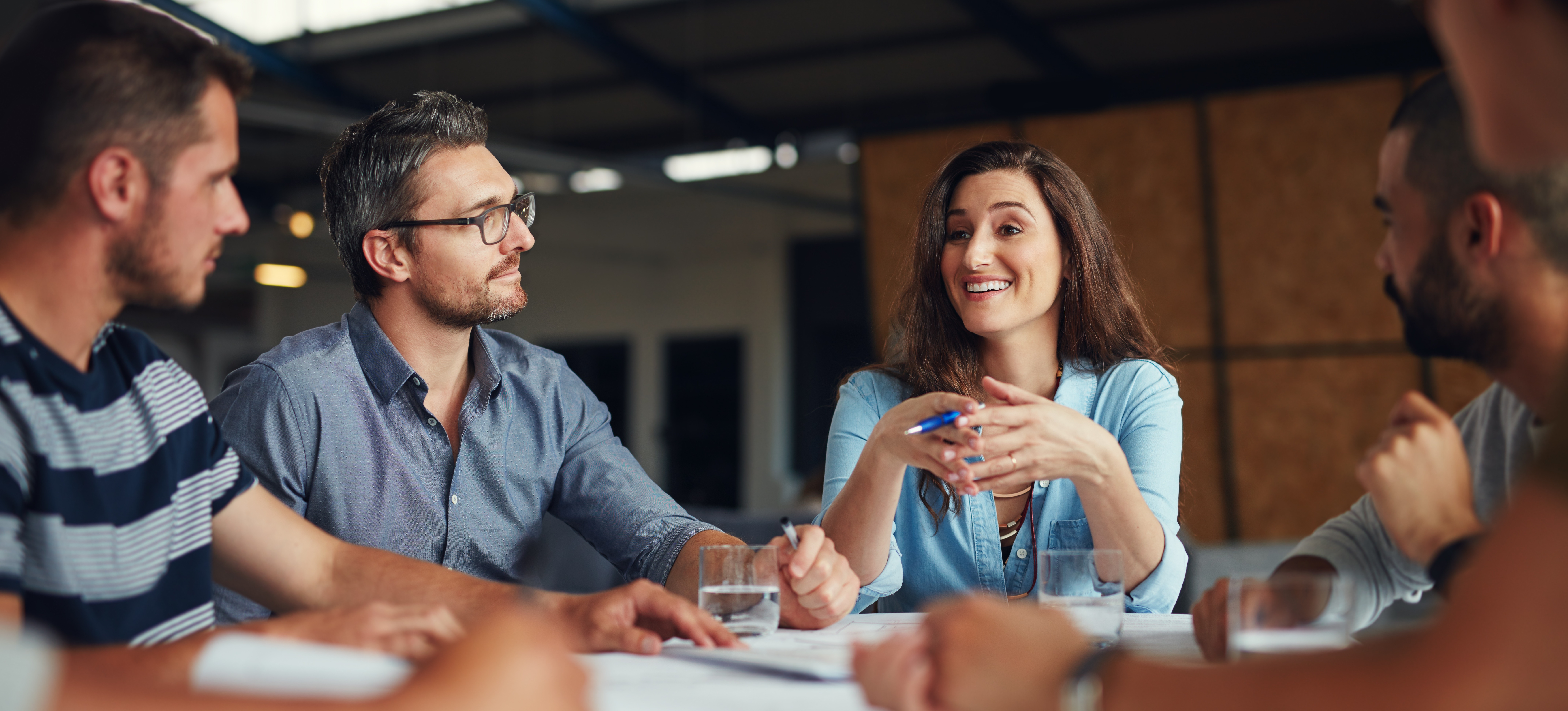 [Image en vedette] Une personne souriante en chemise bleue dirige une réunion d'équipe.
