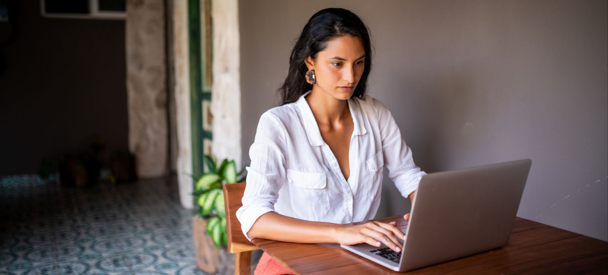 [Featured Image] A woman works on a laptop computer at a wooden table outdoors.