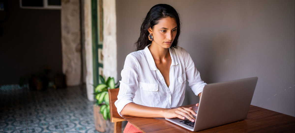 [Featured Image] A woman works on a laptop computer at a wooden table outdoors.