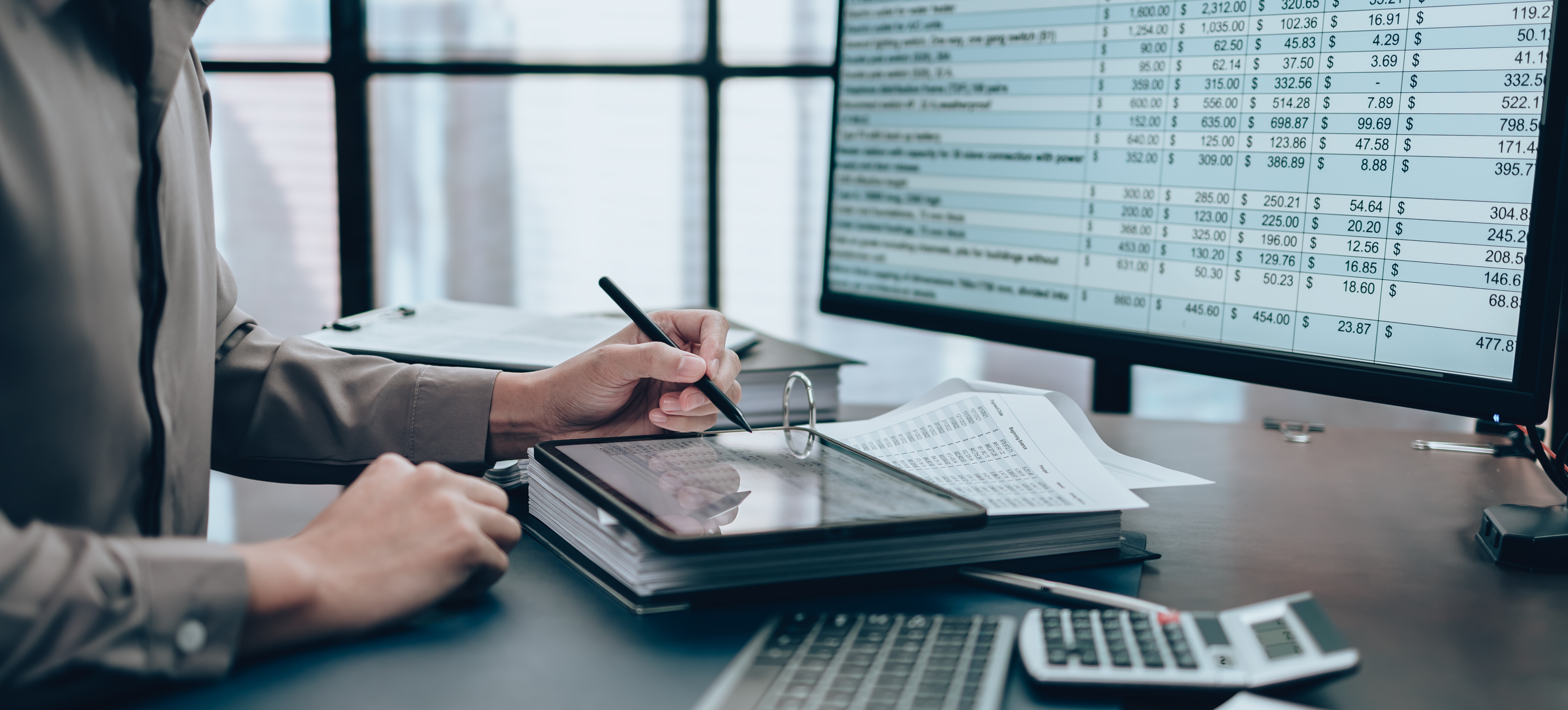 [Featured Image] A business manager who knows how to prepare a balance sheet is working on a spreadsheet at a computer and on a tablet.
