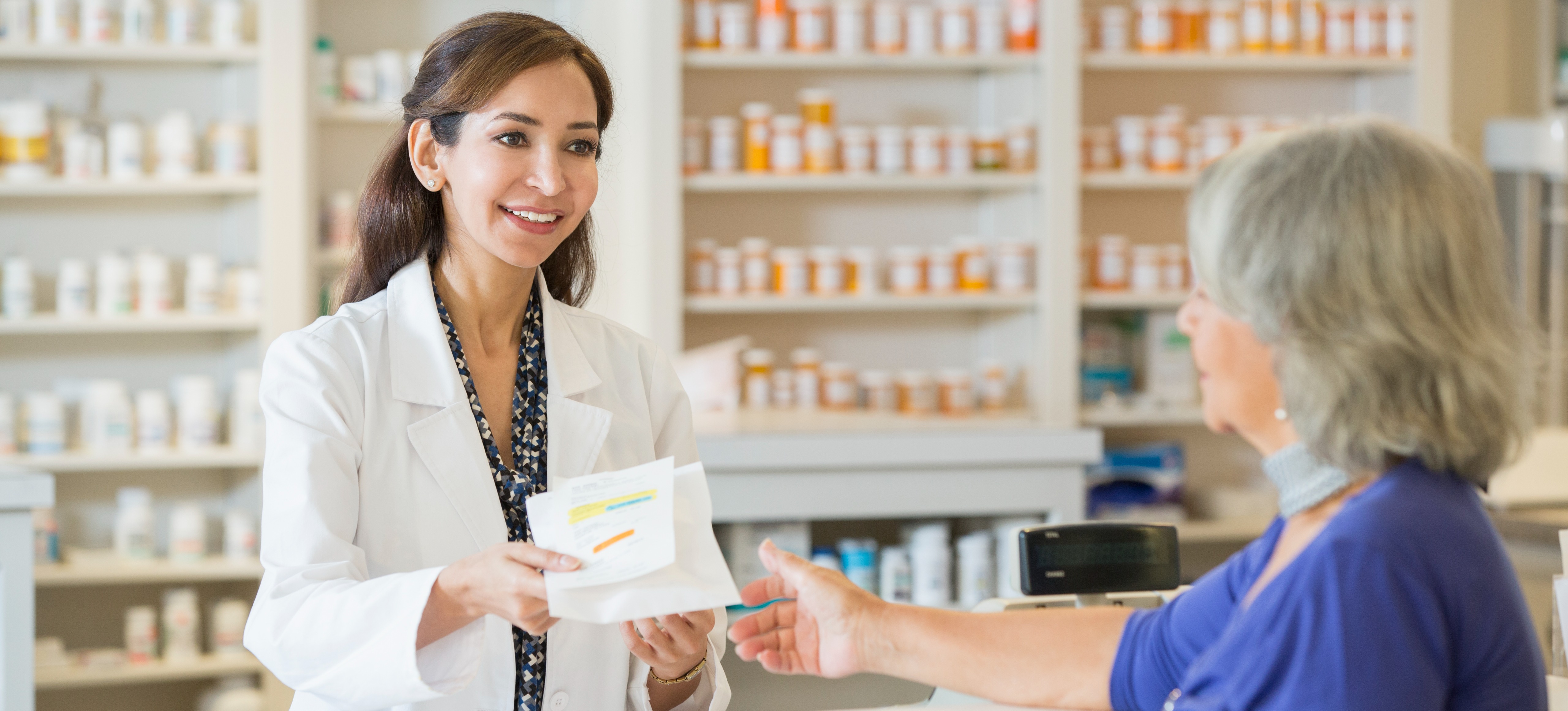 [Featured Image] A pharmacist, one of the high-salary jobs in the science stream, hands a prescription to a customer in a pharmacy. 
