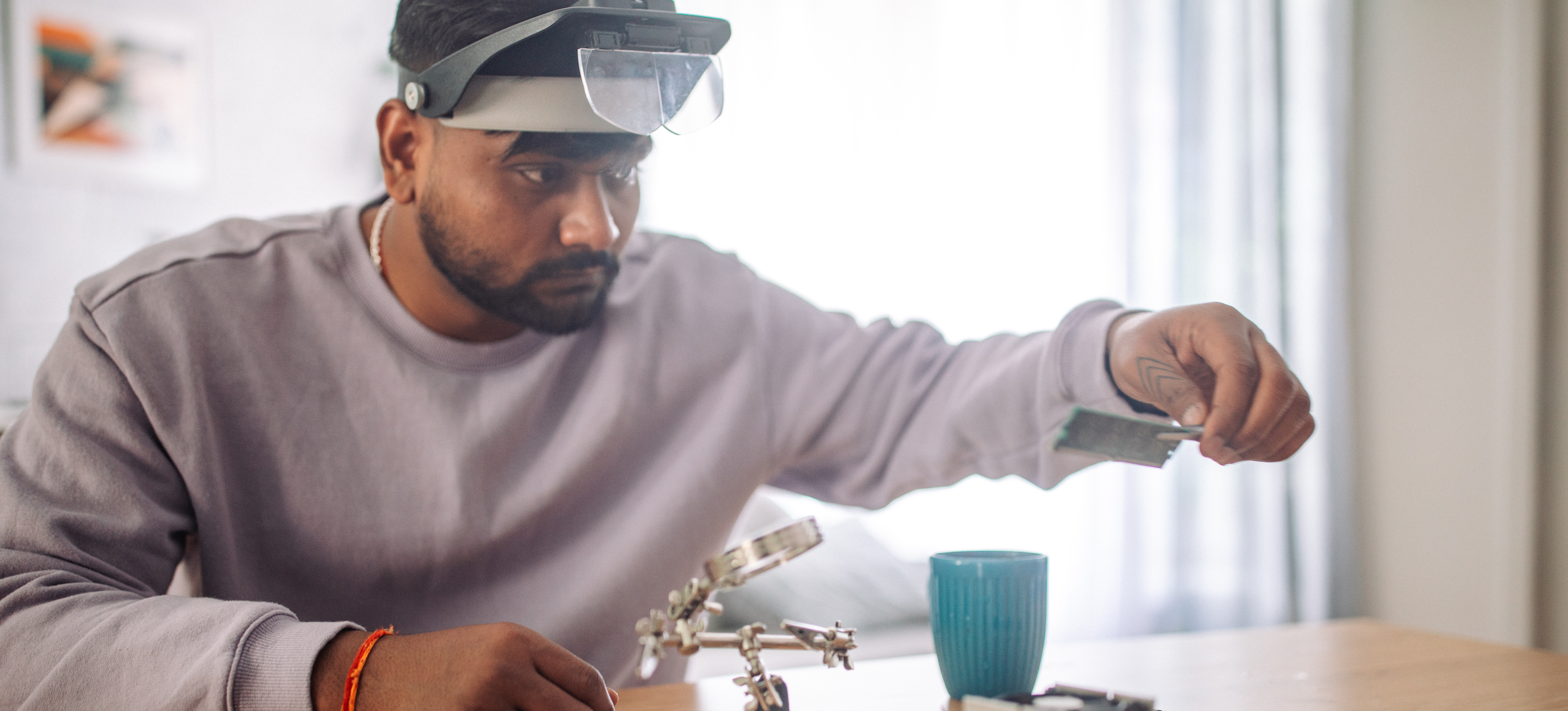 [Featured Image] A computer technician repairs a motherboard in his home office using small tools, a magnifying glass, and a headlamp visor.
