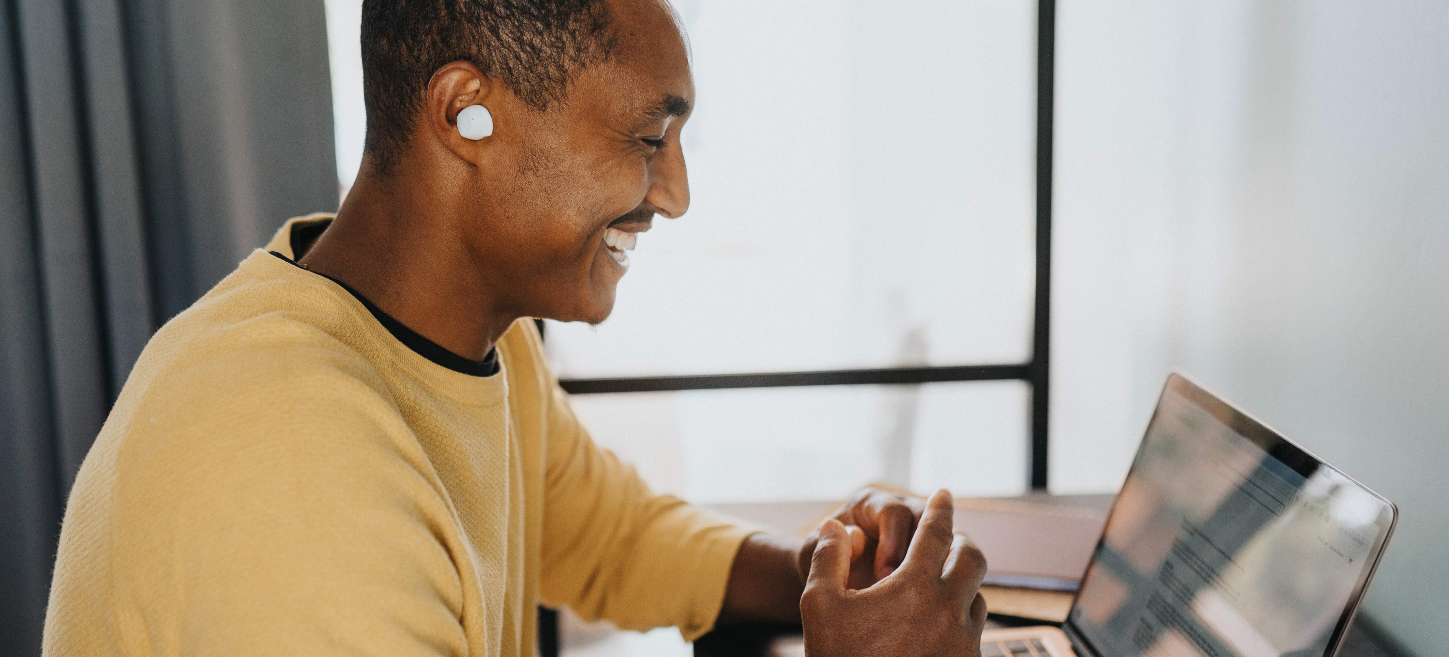 [Featured Image] A business professional smiles at their laptop while reviewing the new app they created using no-code app builders. 
