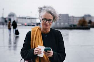 [Featured image] An IT support specialist is reading about MAC addresses on their phone while walking and holding a mug. 