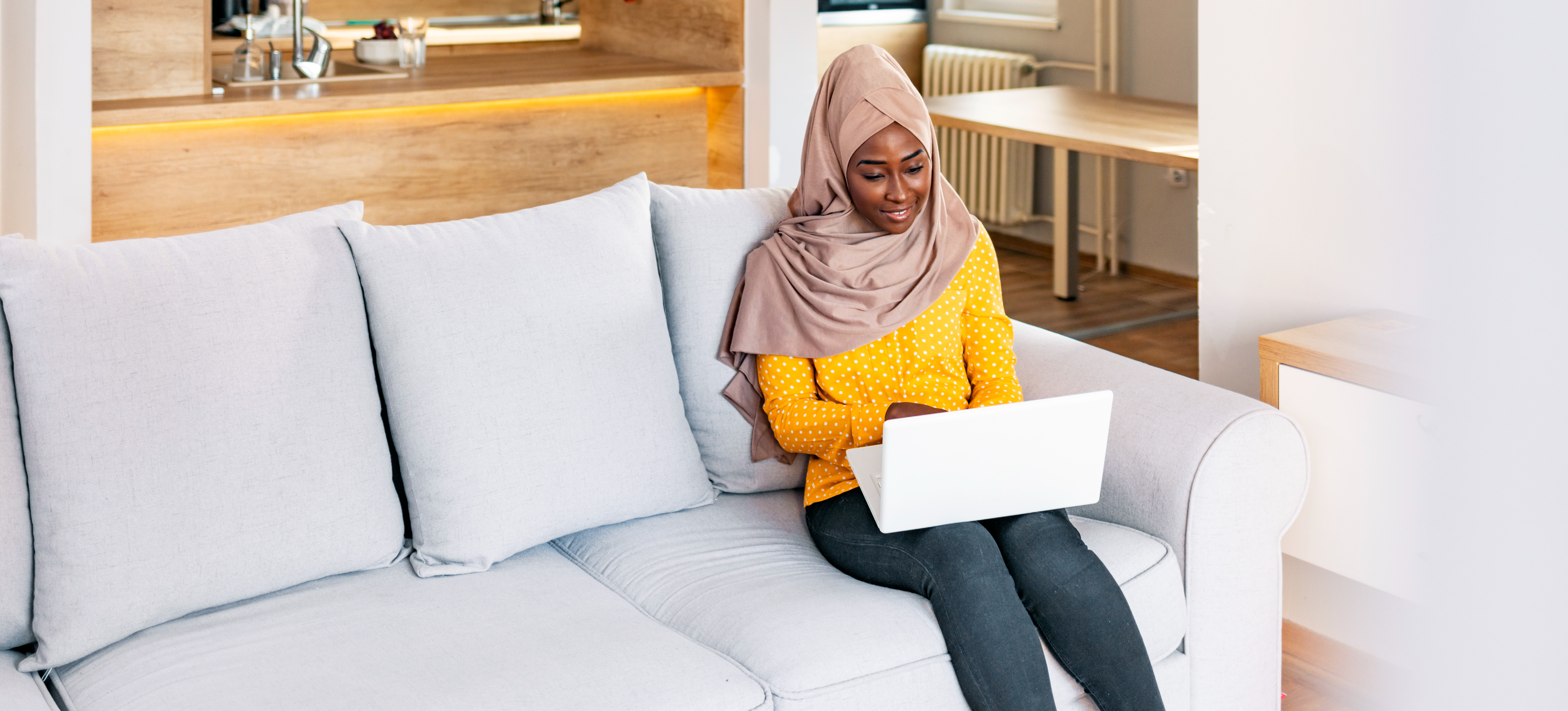 [Featured image] A woman sits on her sofa in her living room working on her resume on her laptop computer.