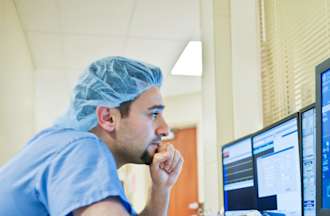 [Featured Image]:  A case manager, wearing a blue uniform and a blue head covering, is sitting in front of three computer screens, looking at charts. 