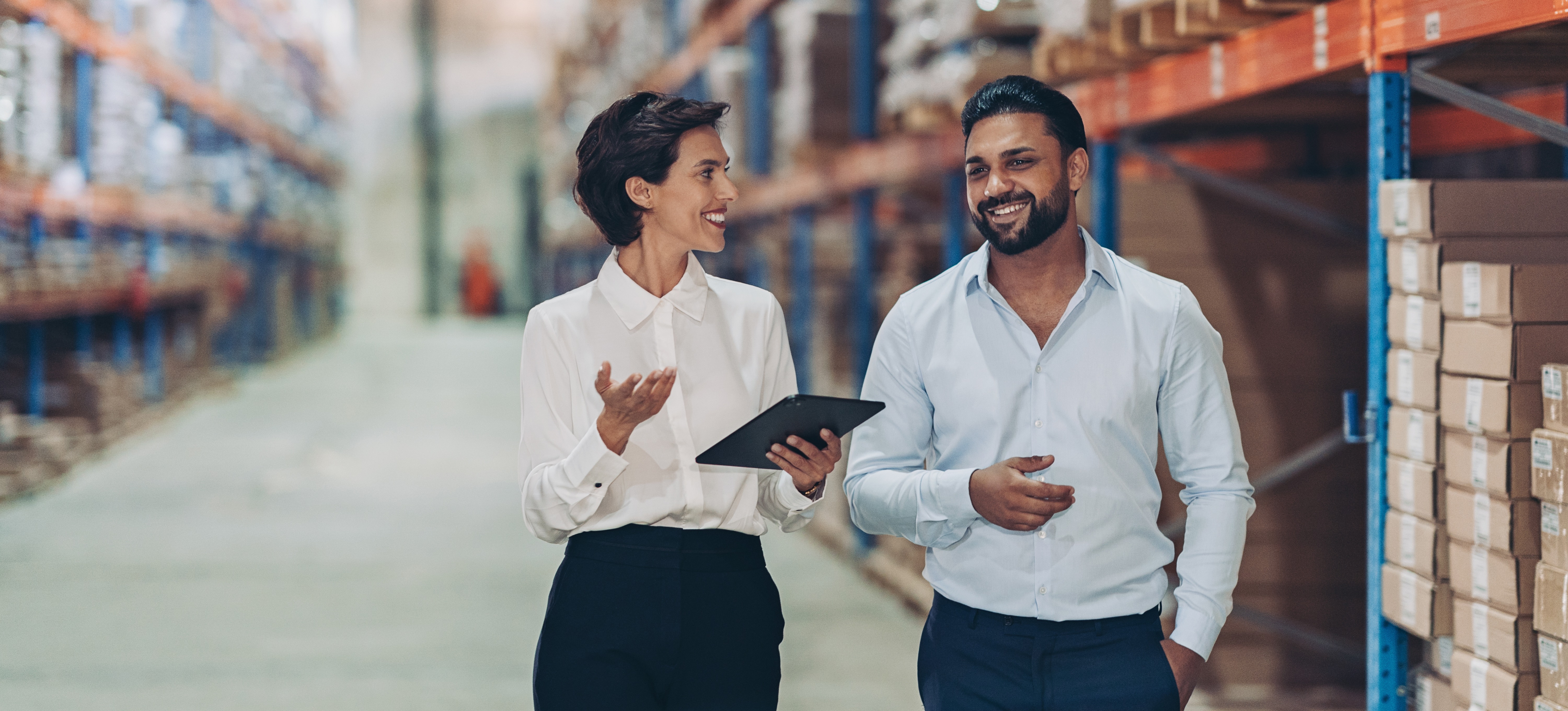 [Featured Image] A businessperson is walking in a warehouse with a colleague who is holding a tablet displaying a Google Sheets pivot table.