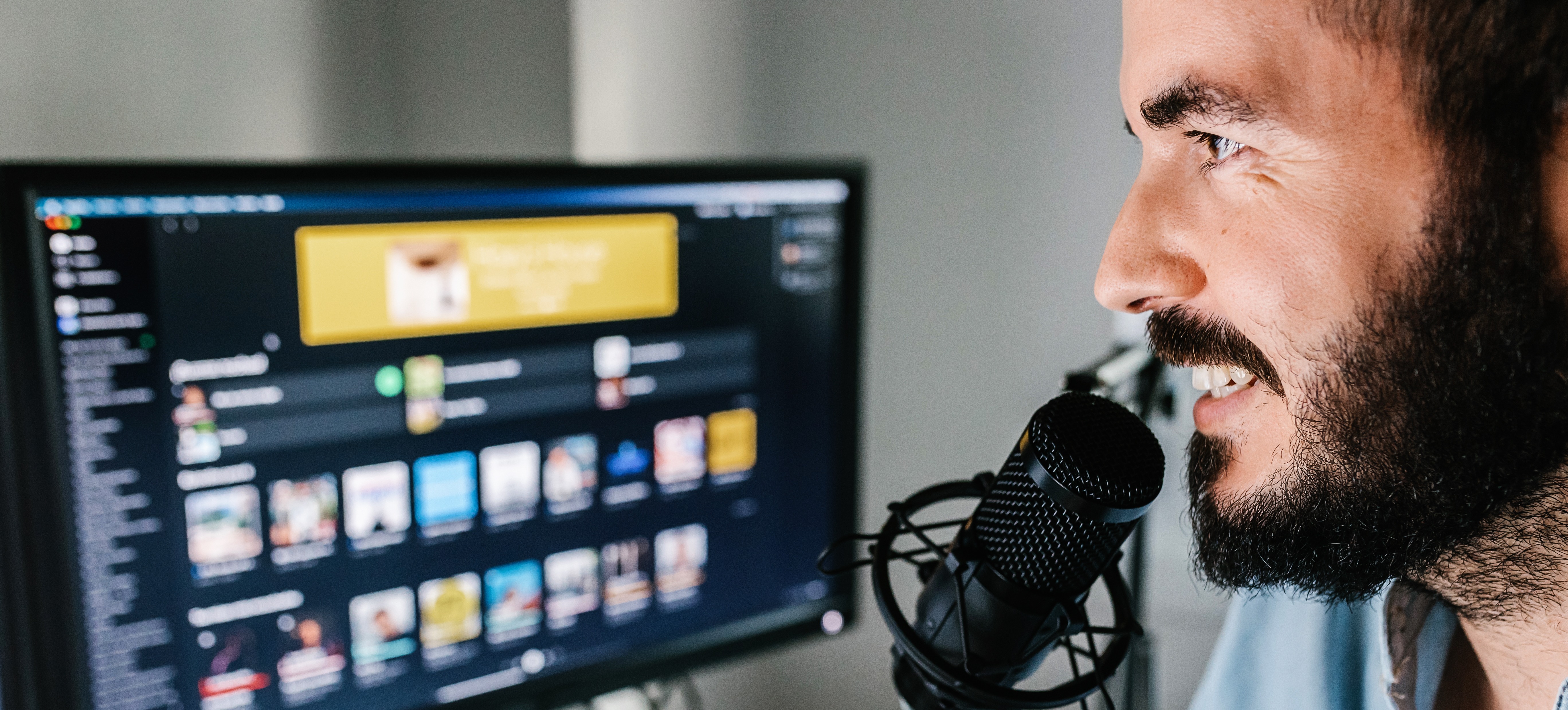 [Featured Image] A person using a microphone and sitting in front of their computer screen uses their digital content creator skills to record a podcast.