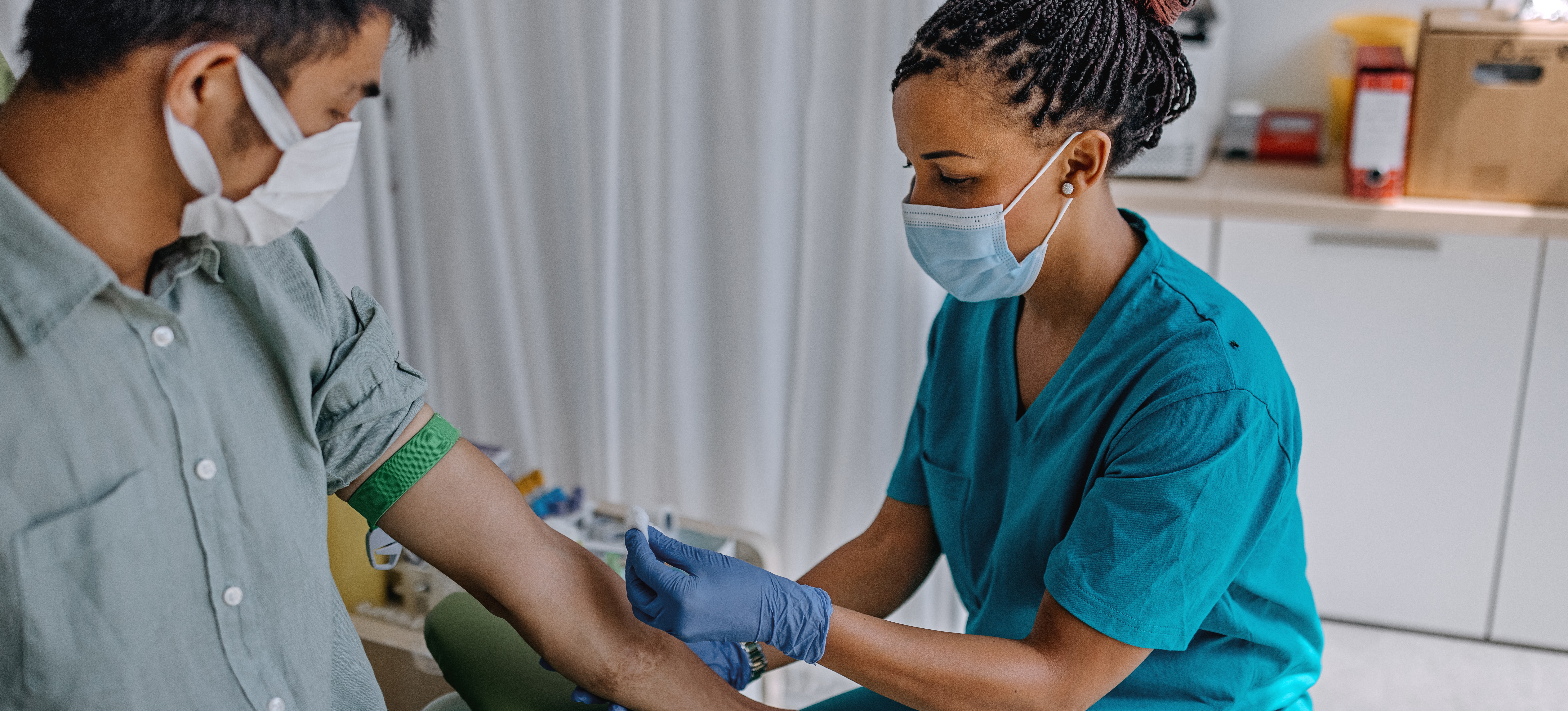 [Featured Image] A phlebotomist wearing scrubs draws blood from a patient in a hospital.