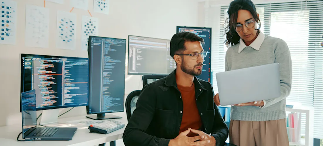 [Featured Image] Two iOS app developers work together to refine software for a new app.
