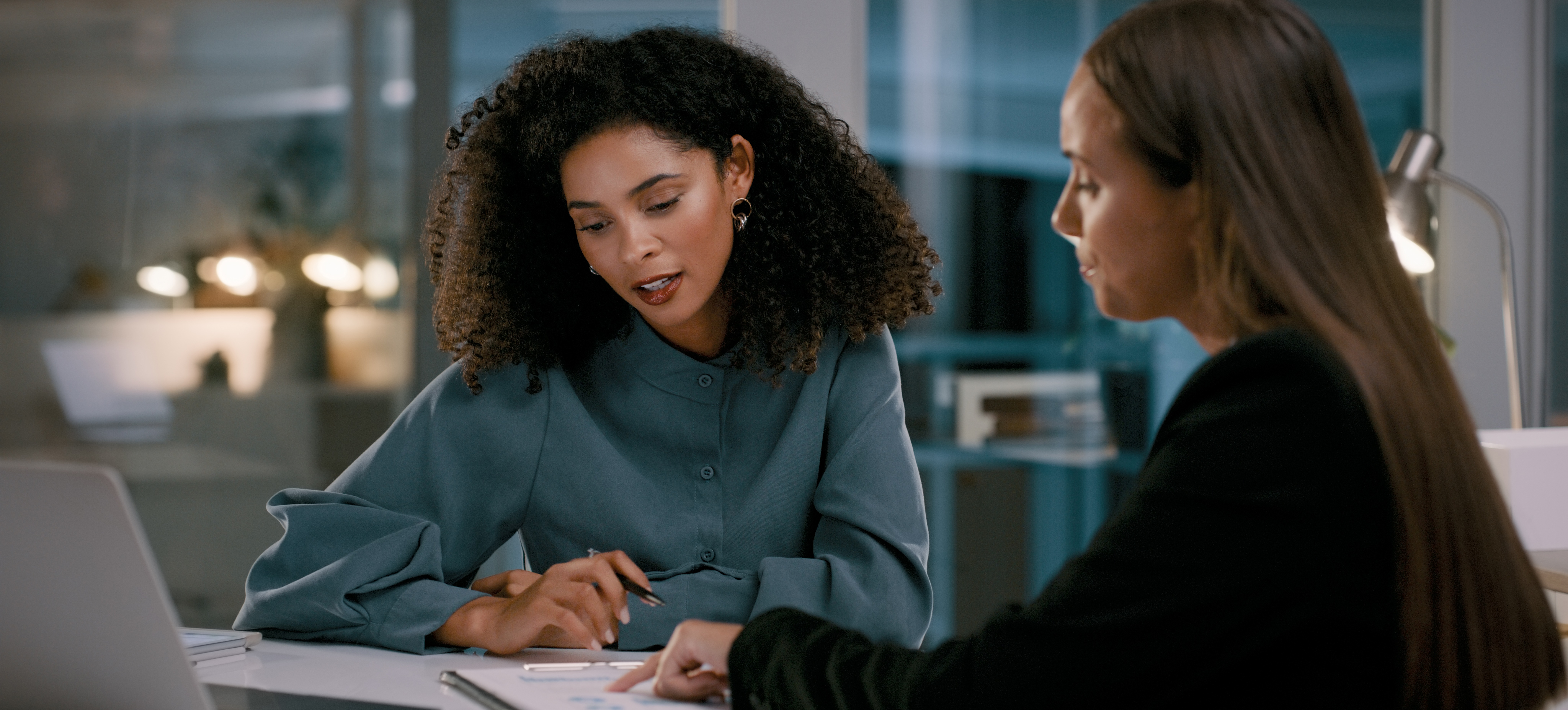 [Hauptbild] Ein Vorgesetzter bespricht mit seinem Mitarbeiter einen Schulungsplan, während beide in einem Büro sitzen und auf ein Klemmbrett und einen Laptop schauen.