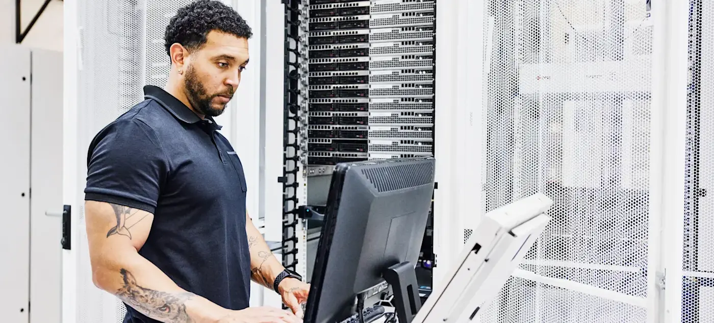 [Featured Image] An application architect is on a computer, building the structural components of an application in the server room.
