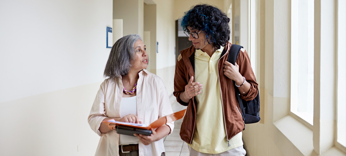 [Featured Image] A young person and their professor walk down a hallway and discuss potential computer science fields they can explore.

