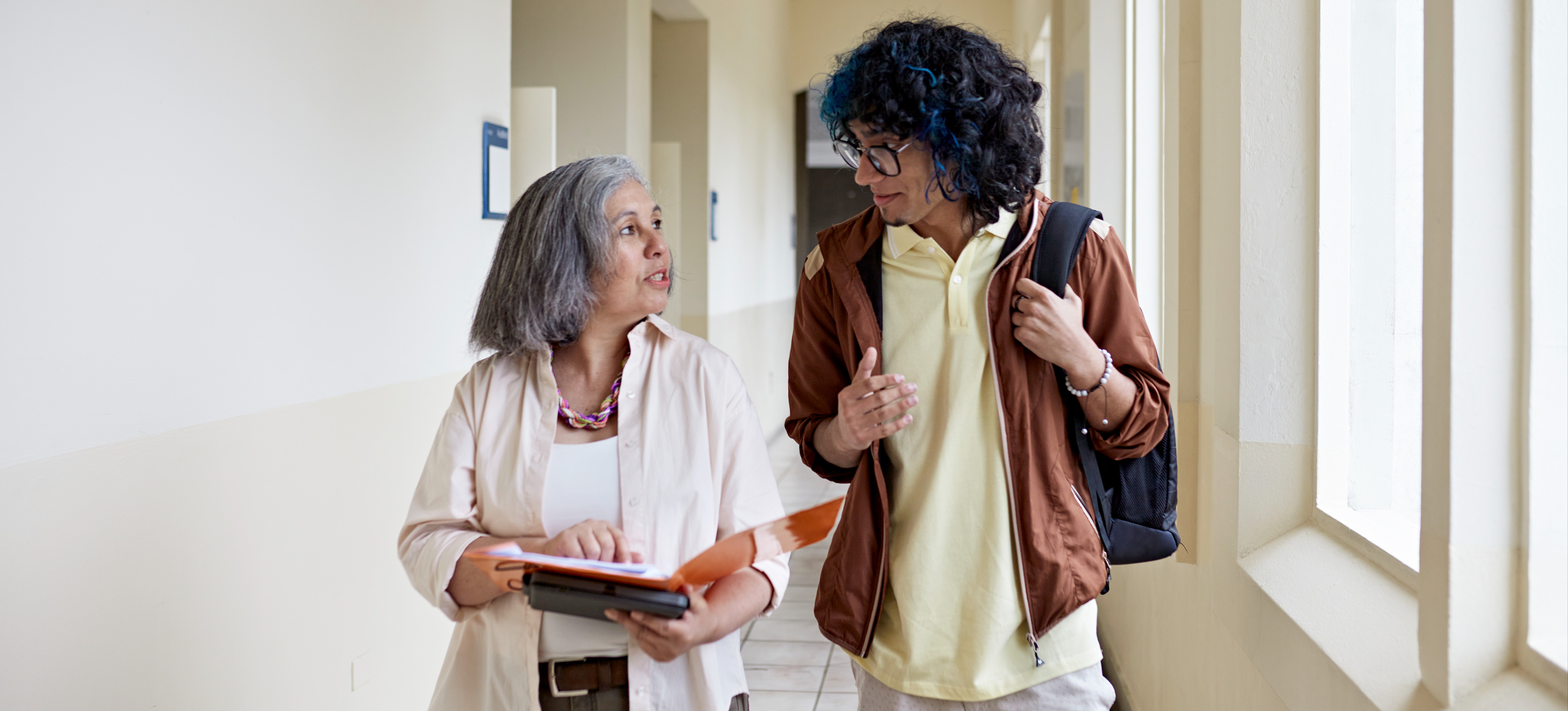 [Featured Image] A young person and their professor walk down a hallway and discuss potential computer science fields they can explore.
