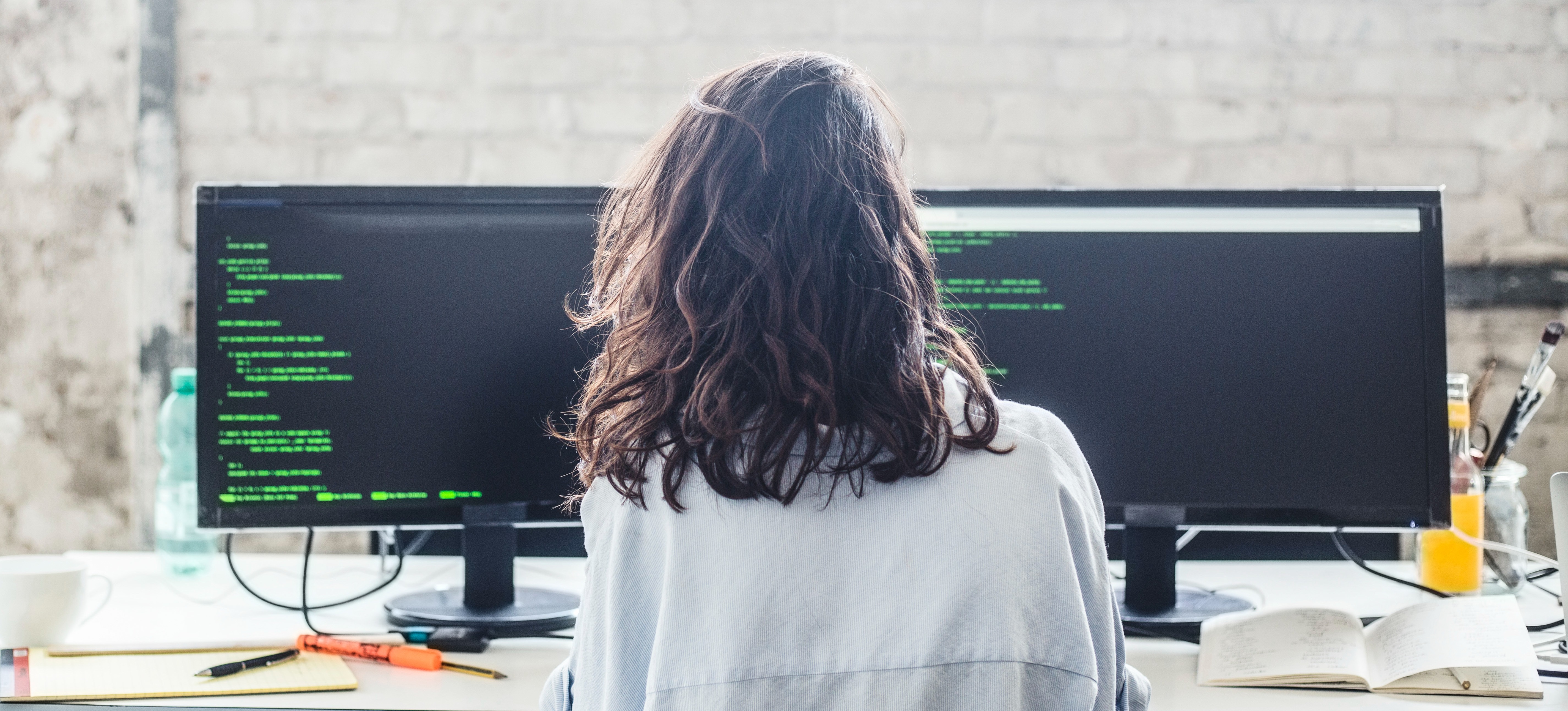 [Featured image] A computer engineer is coding on two computer screens. 