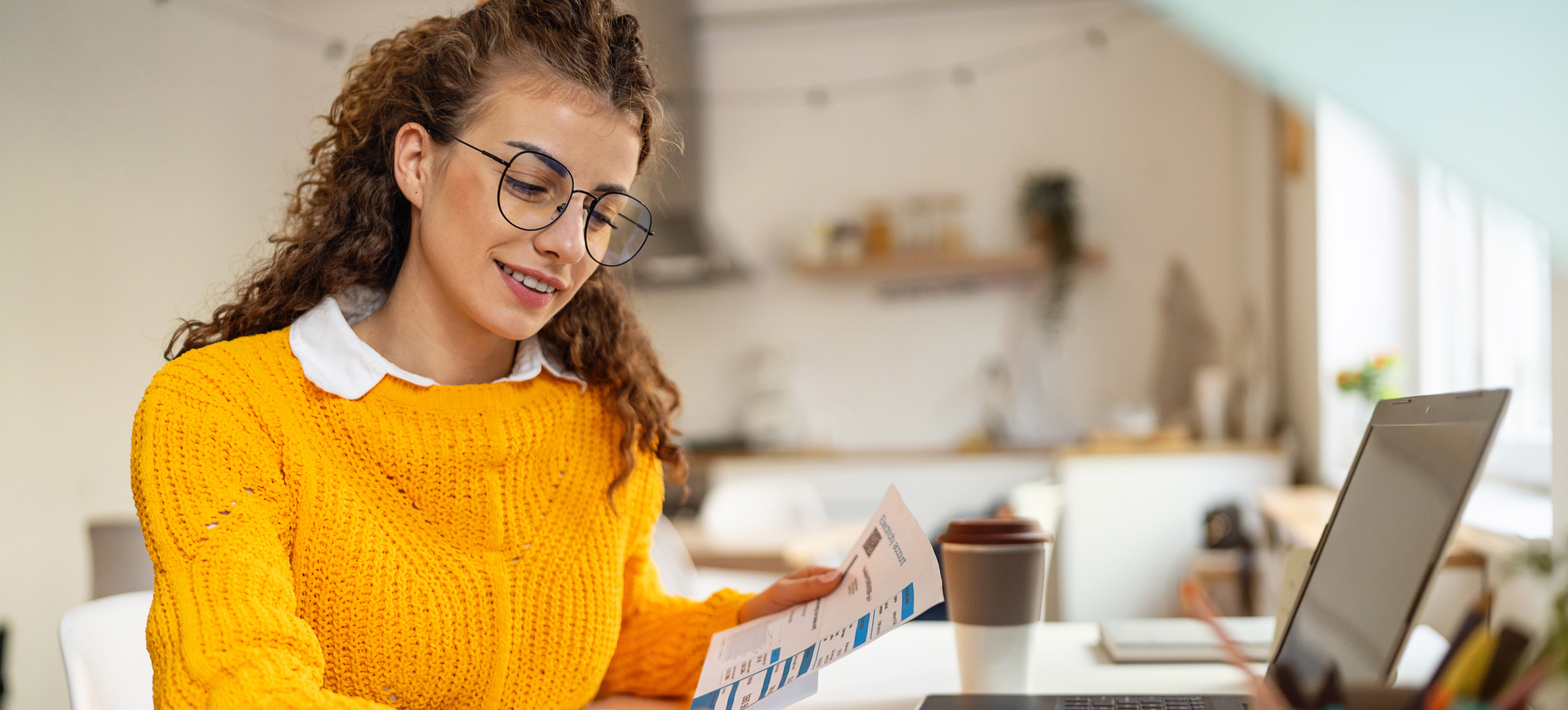 [Featured image] A person with glasses dressed in a yellow sweater studies at home for their online accounting degree using their laptop, calculator, and papers. 
