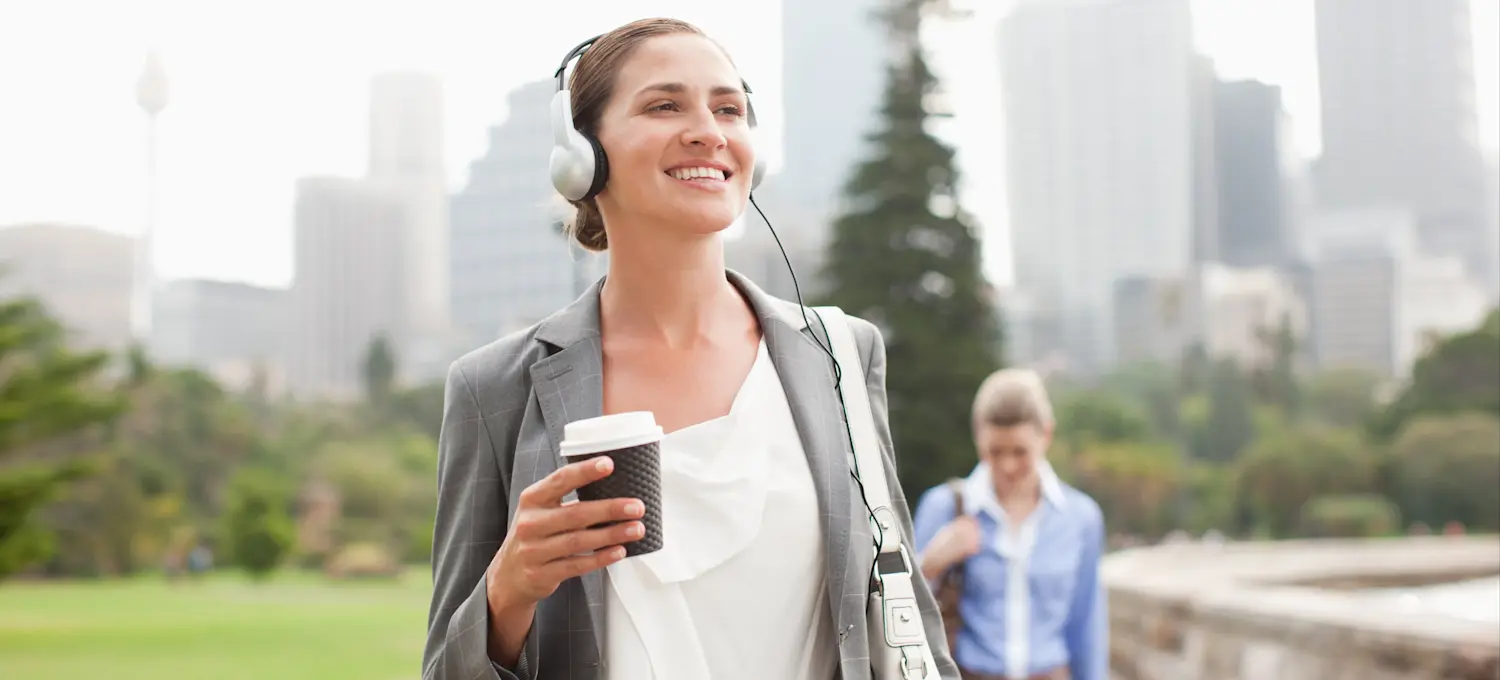 [Featured Image] A person holding coffee and listening to headphones walks to work in one of the best cities for cybersecurity jobs.